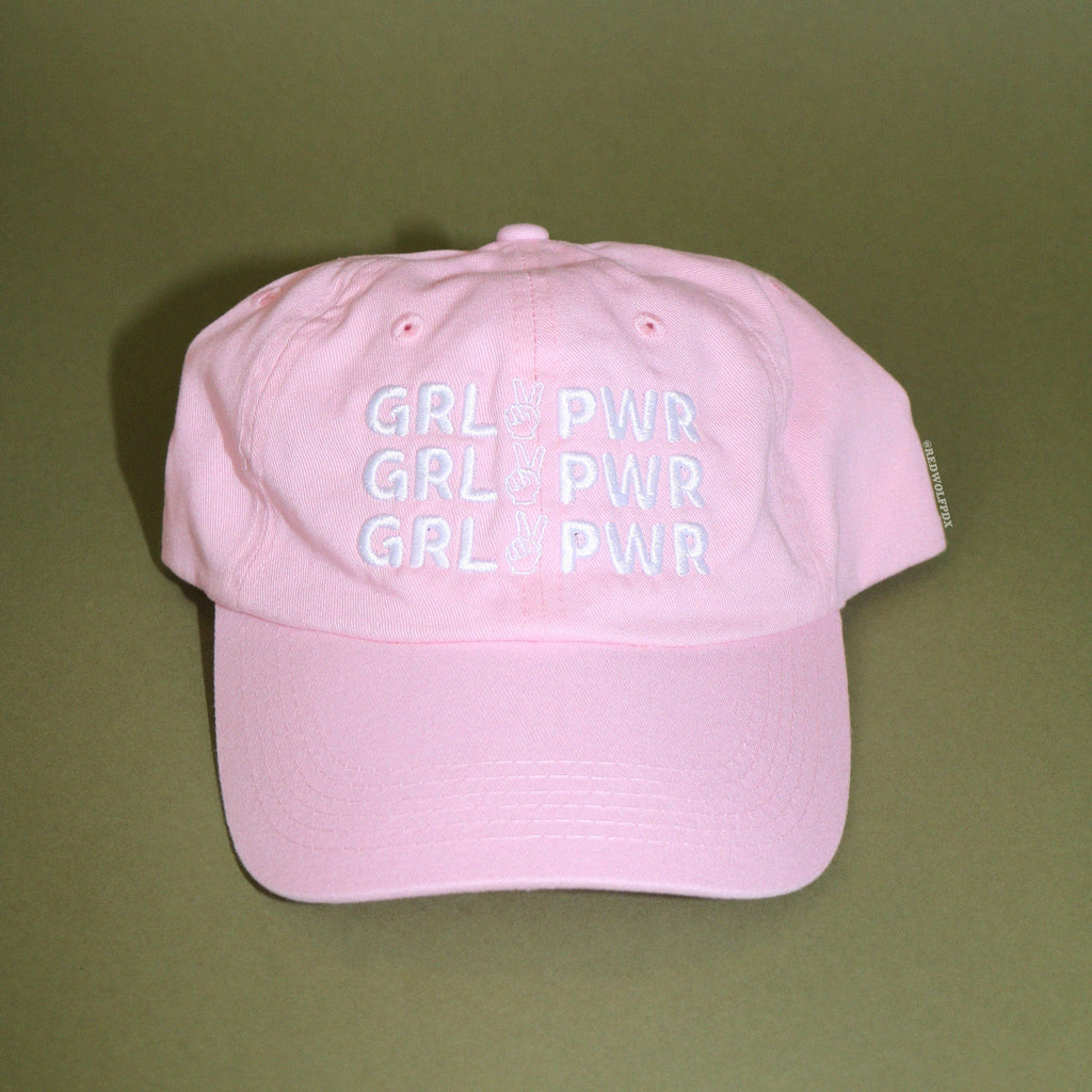 Pink baseball cap with text 'GRL PWR' embroidered in white thread across front on a green backdrop