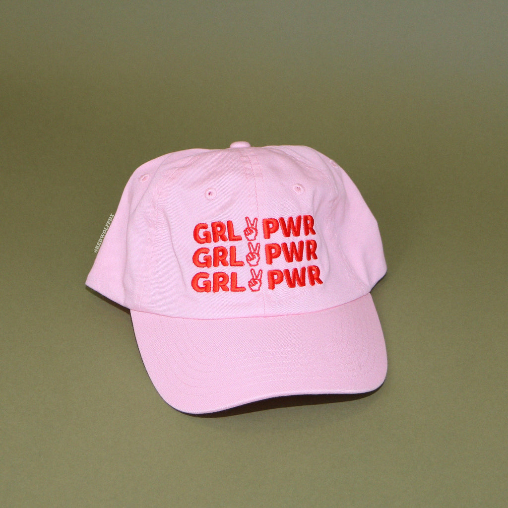 light pink baseball cap with red thread embroidered text 'GRL PWR' across front on a vintage green backdrop