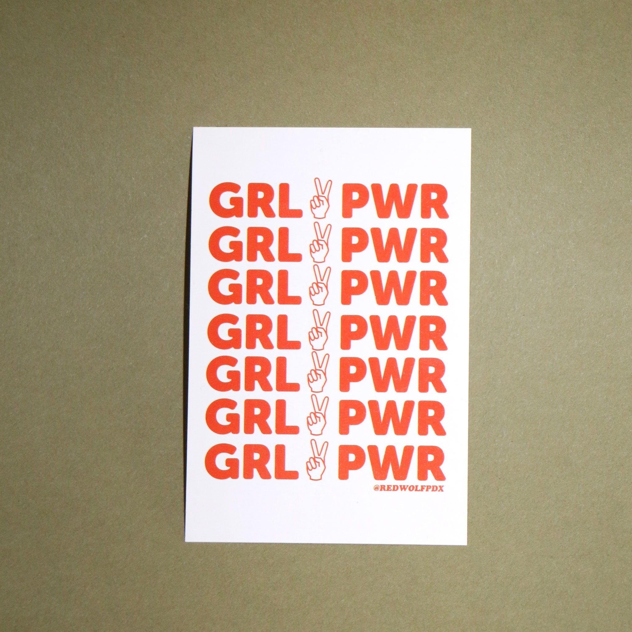 red orange text 'GRL PWR' graphic on white rectangle sticker background on a vintage green backdrop