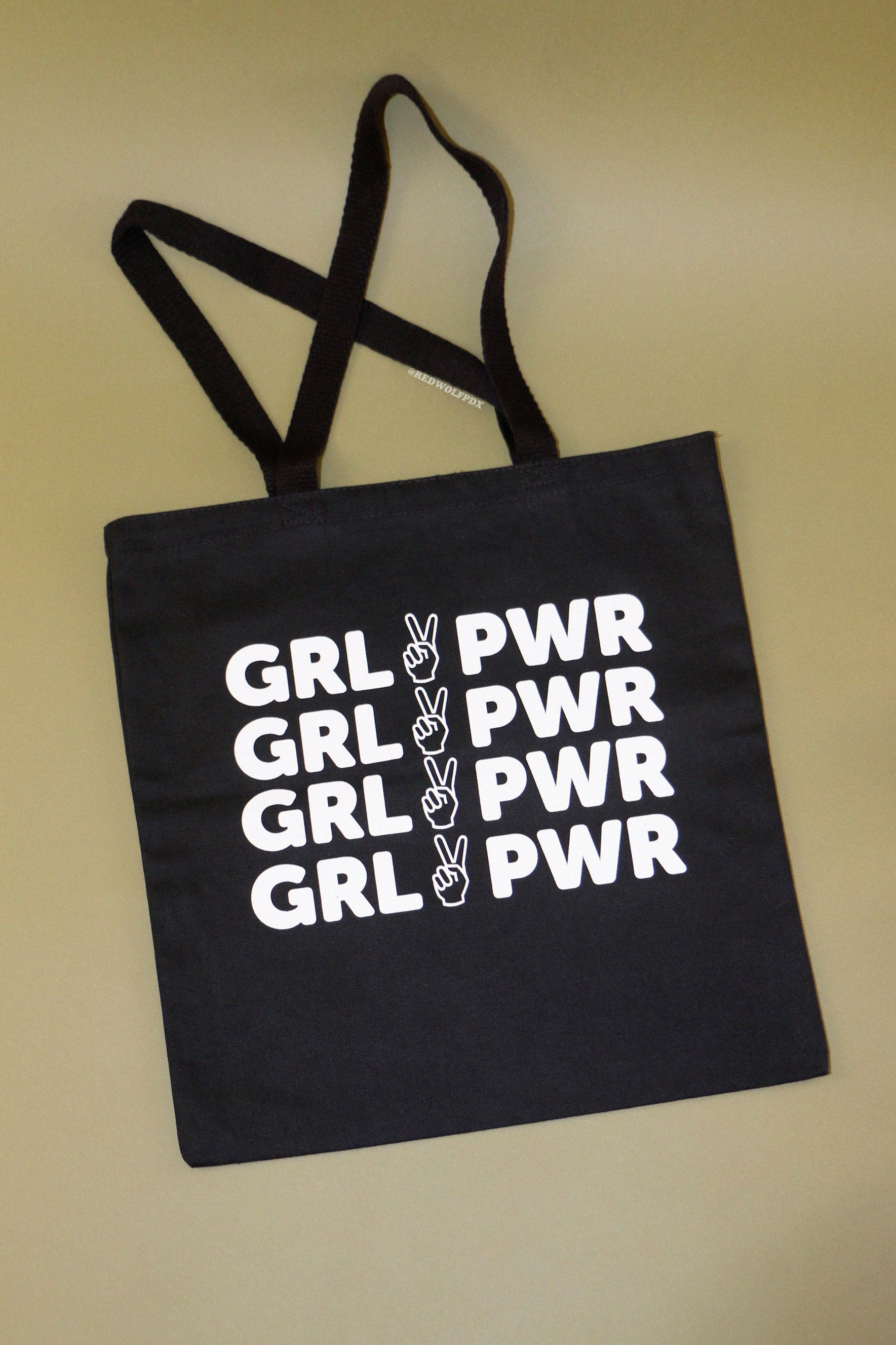 Black canvas tote bag with text 'GRL PWR' in white ink screen printed across against a vintage green backdrop
