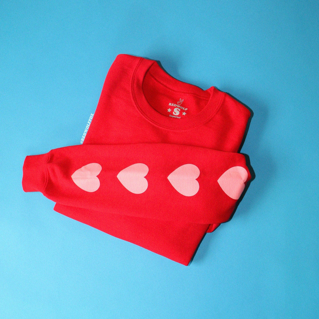 heart printed sleeves on red crewneck sweatshirt folded on blue backdrop