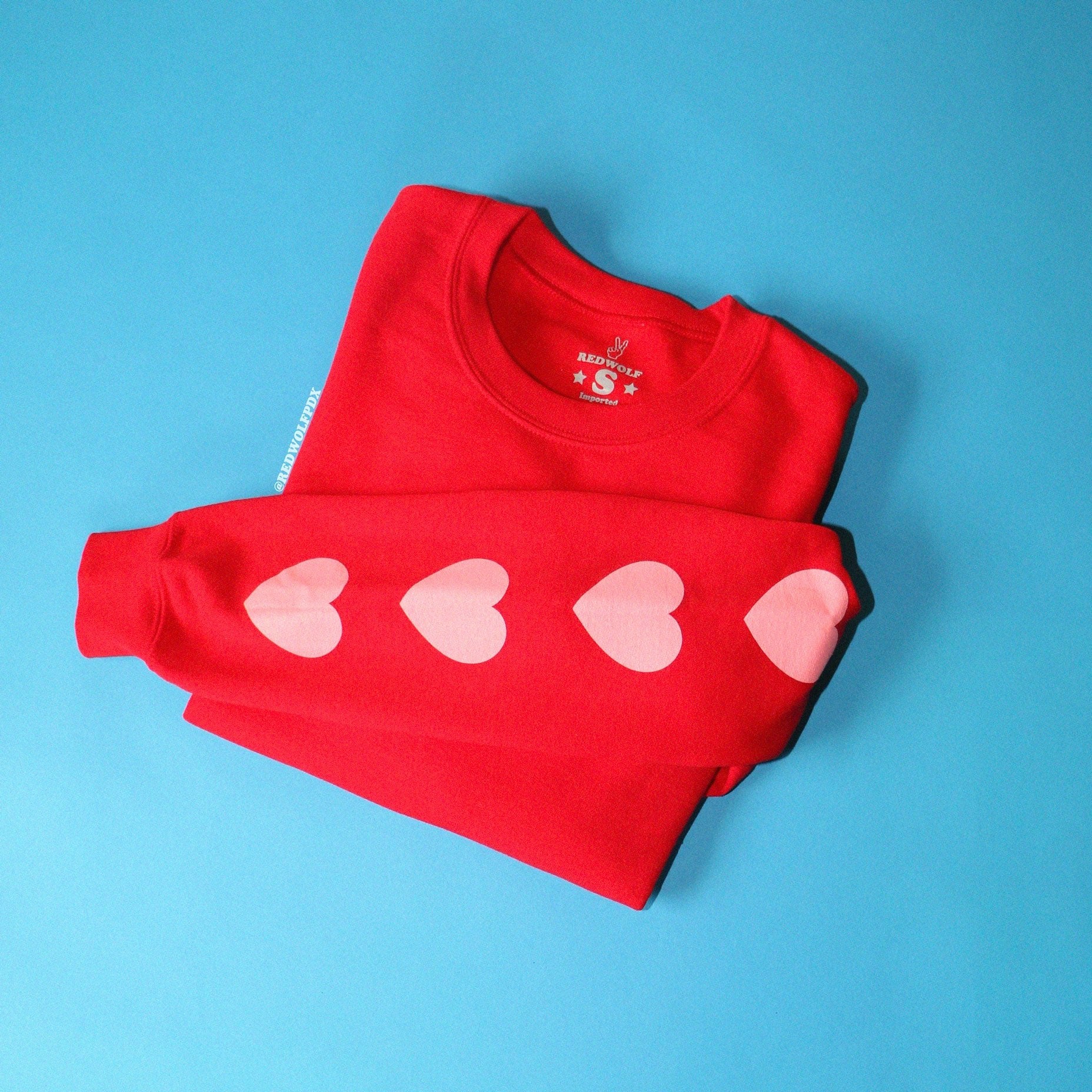 heart printed sleeves on red crewneck sweatshirt folded on blue backdrop