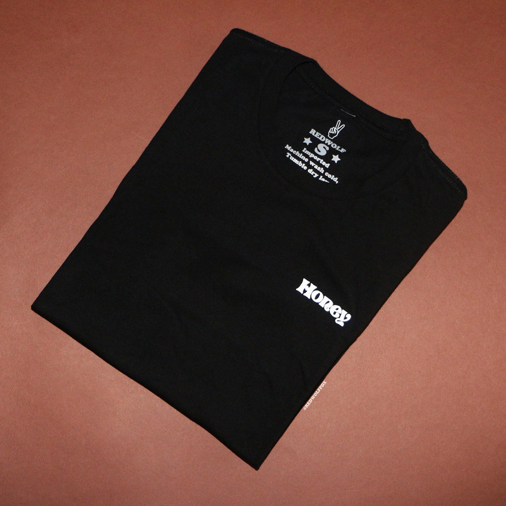 Folded black tee with the text 'Honey' against brown backdrop