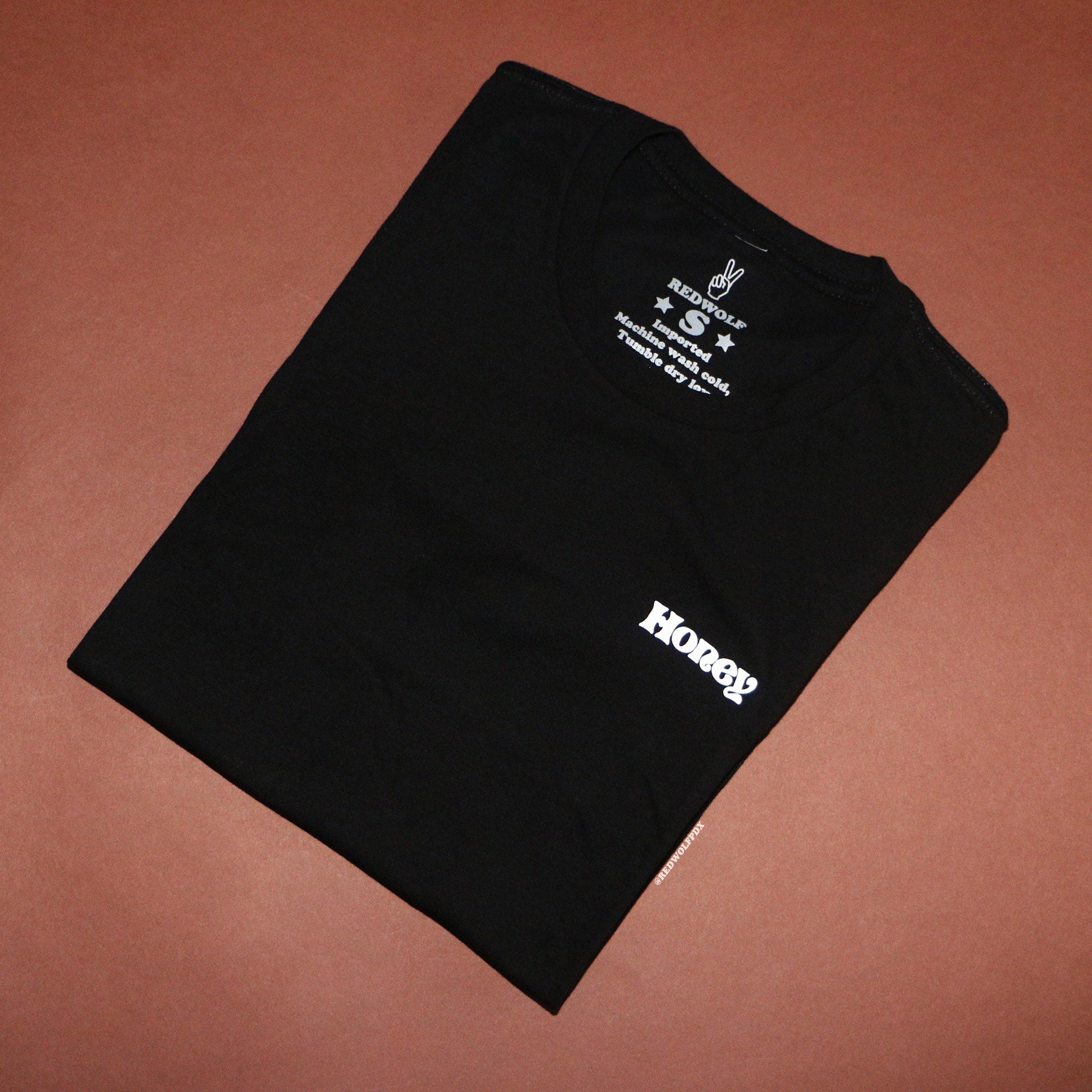 Folded black tee with the text 'Honey' against brown backdrop