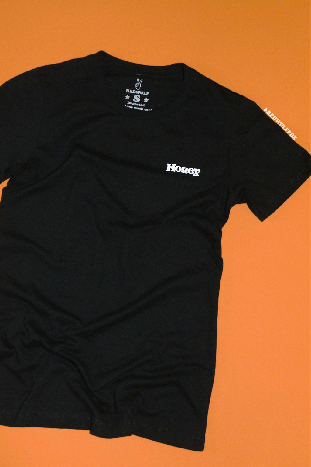 Black t-shirt with text 'Honey' graphic on front corner of chest against a vintage orange background