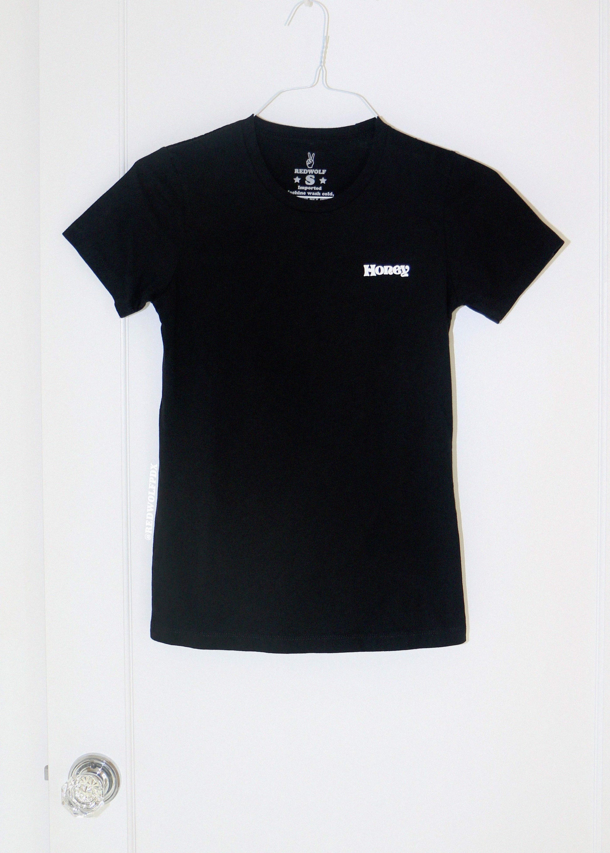 Black t-shirt with  text 'Honey' hanging on on a white door