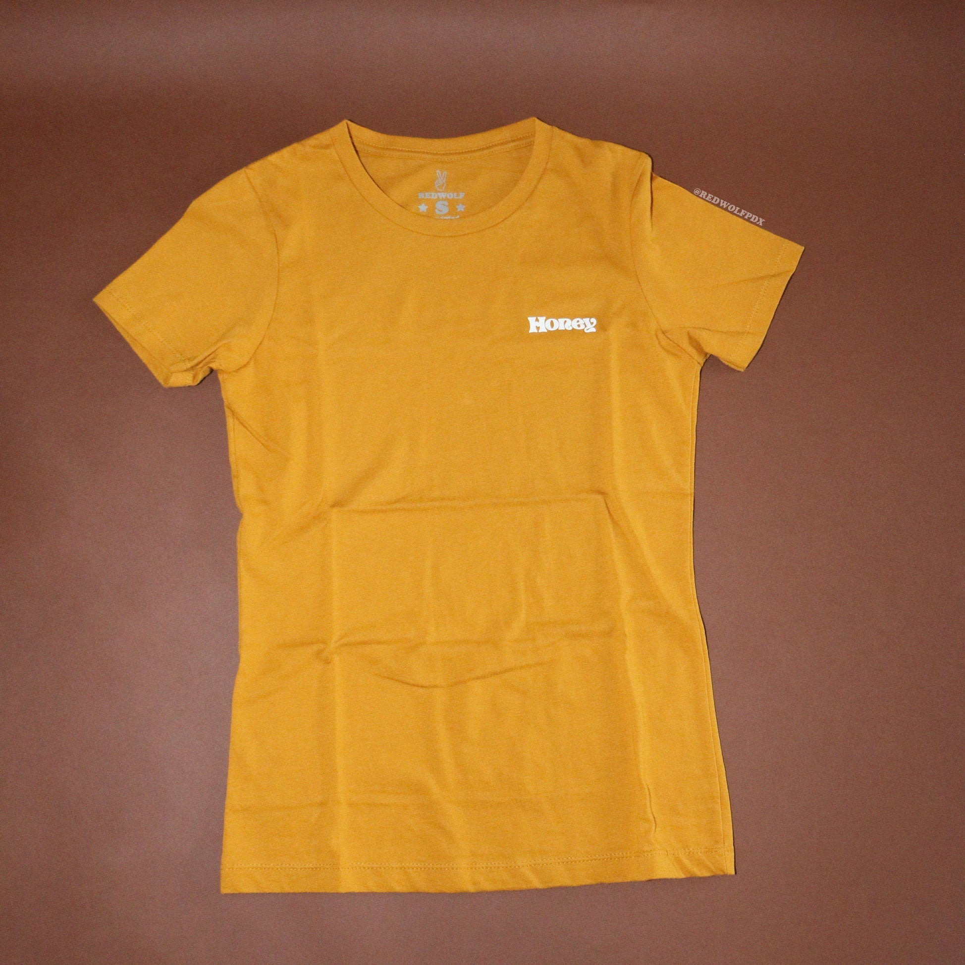 Golden yellow fitted graphic tee with text 'Honey' on front corner chest on a brown background