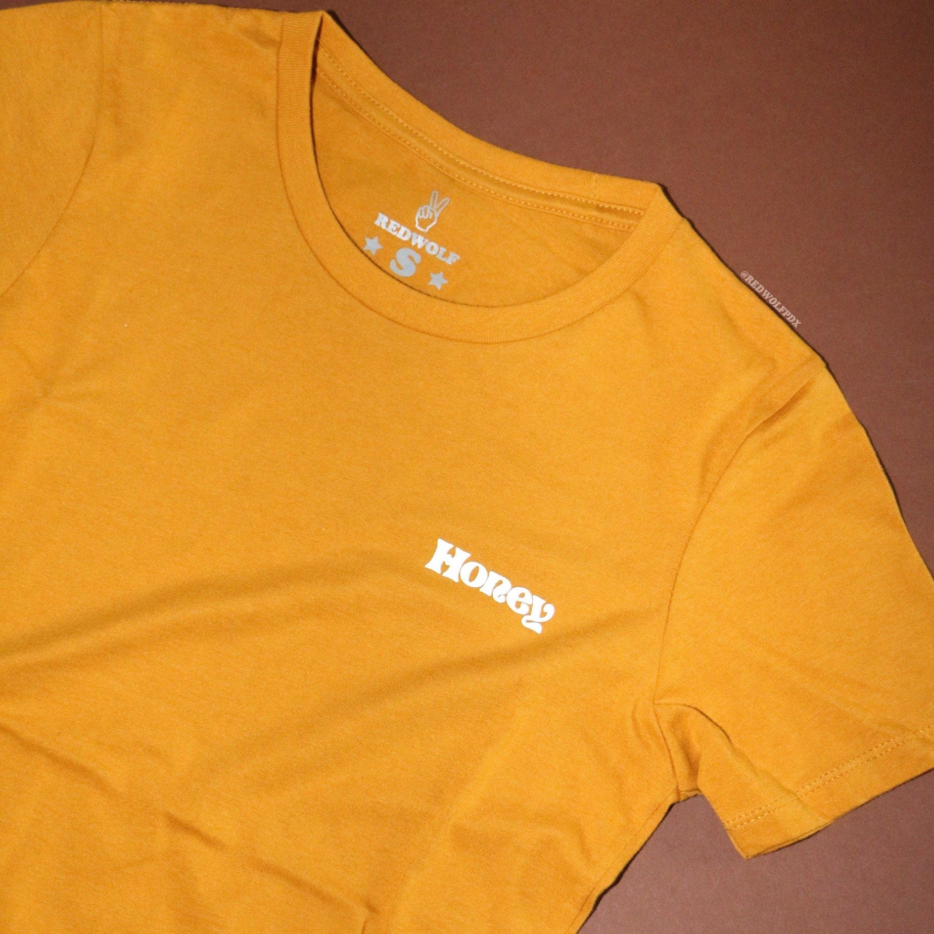 Vintage golden yellow graphic tee with text 'Honey' white ink screen printed on front corner chest on a brown background