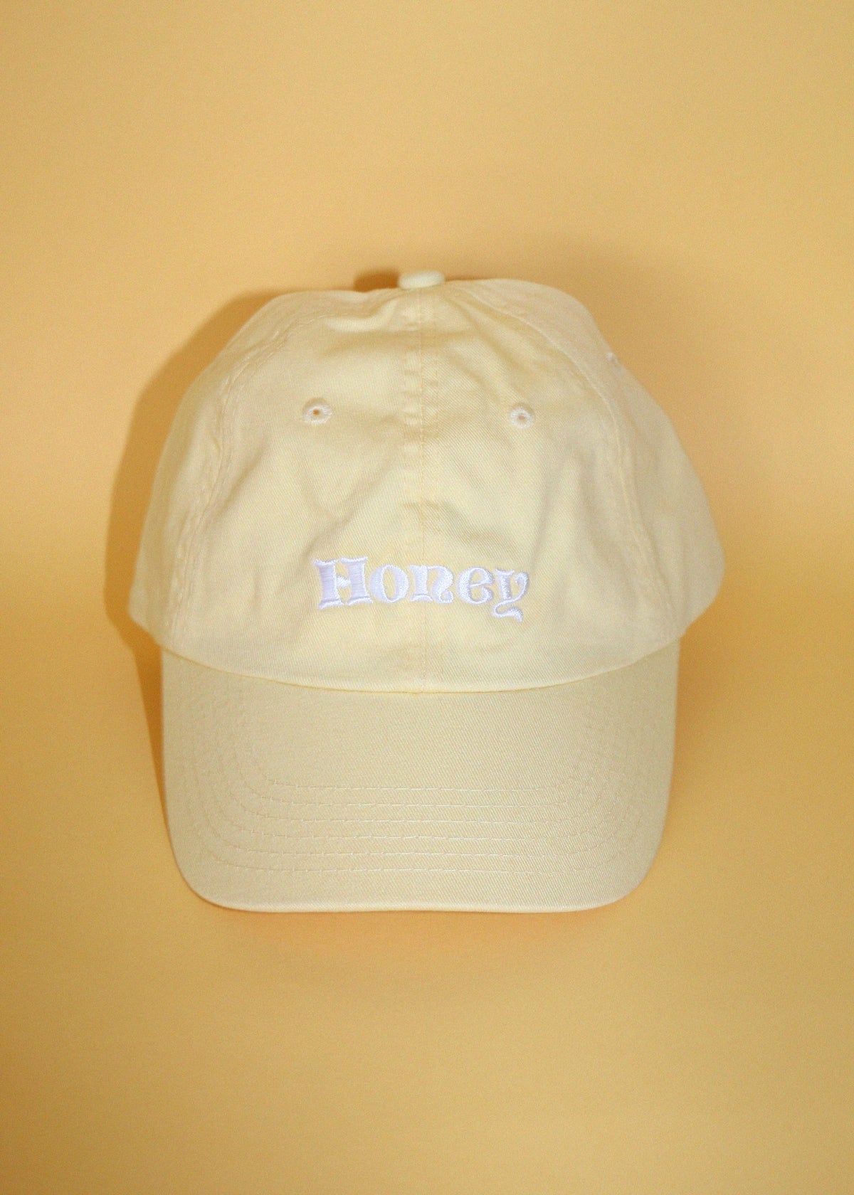 butter yellow baseball cap with text 'Honey' embroidered in white thread against a yellow backdrop.