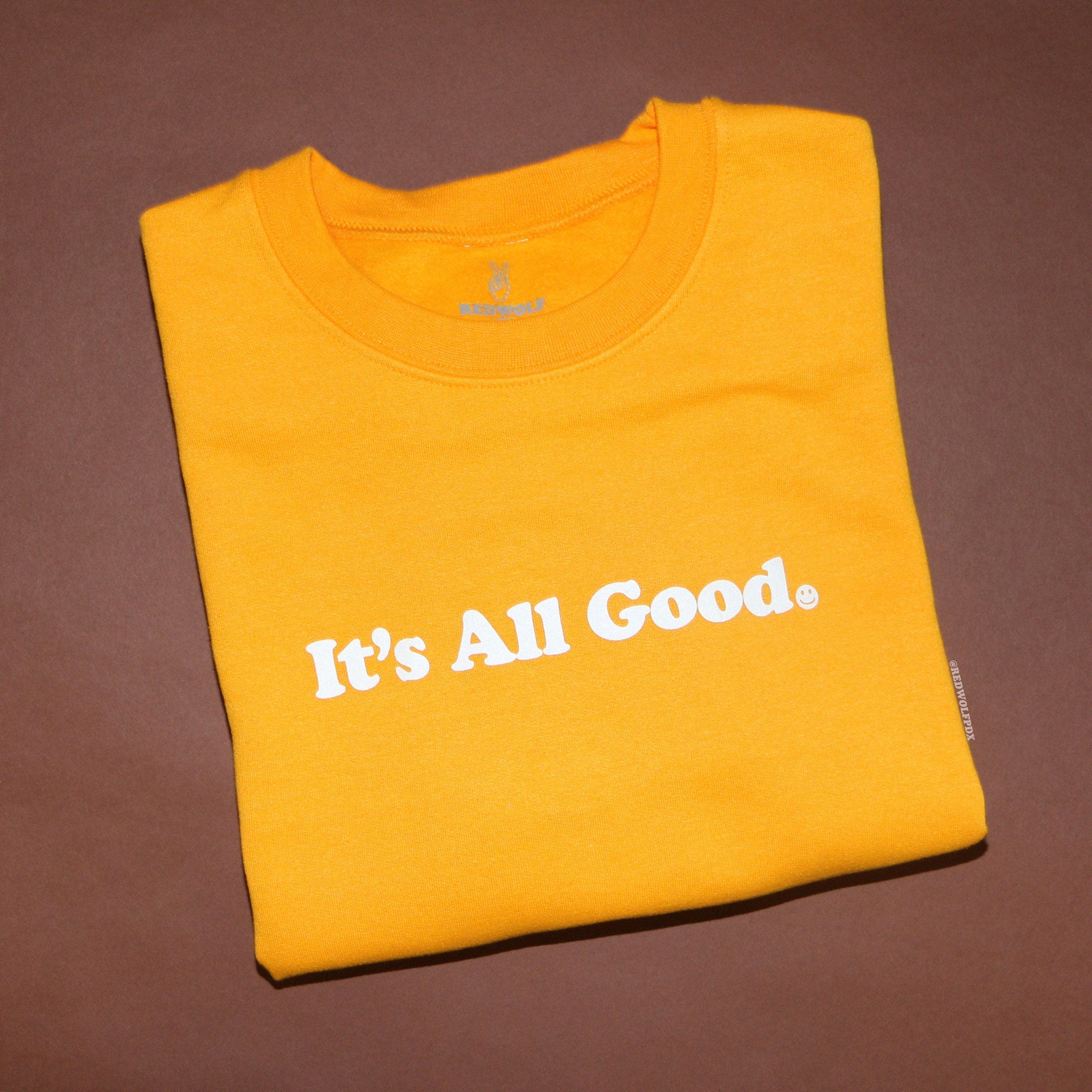 yellow crewneck sweatshirt with it's all good graphic folded on brown backdrop