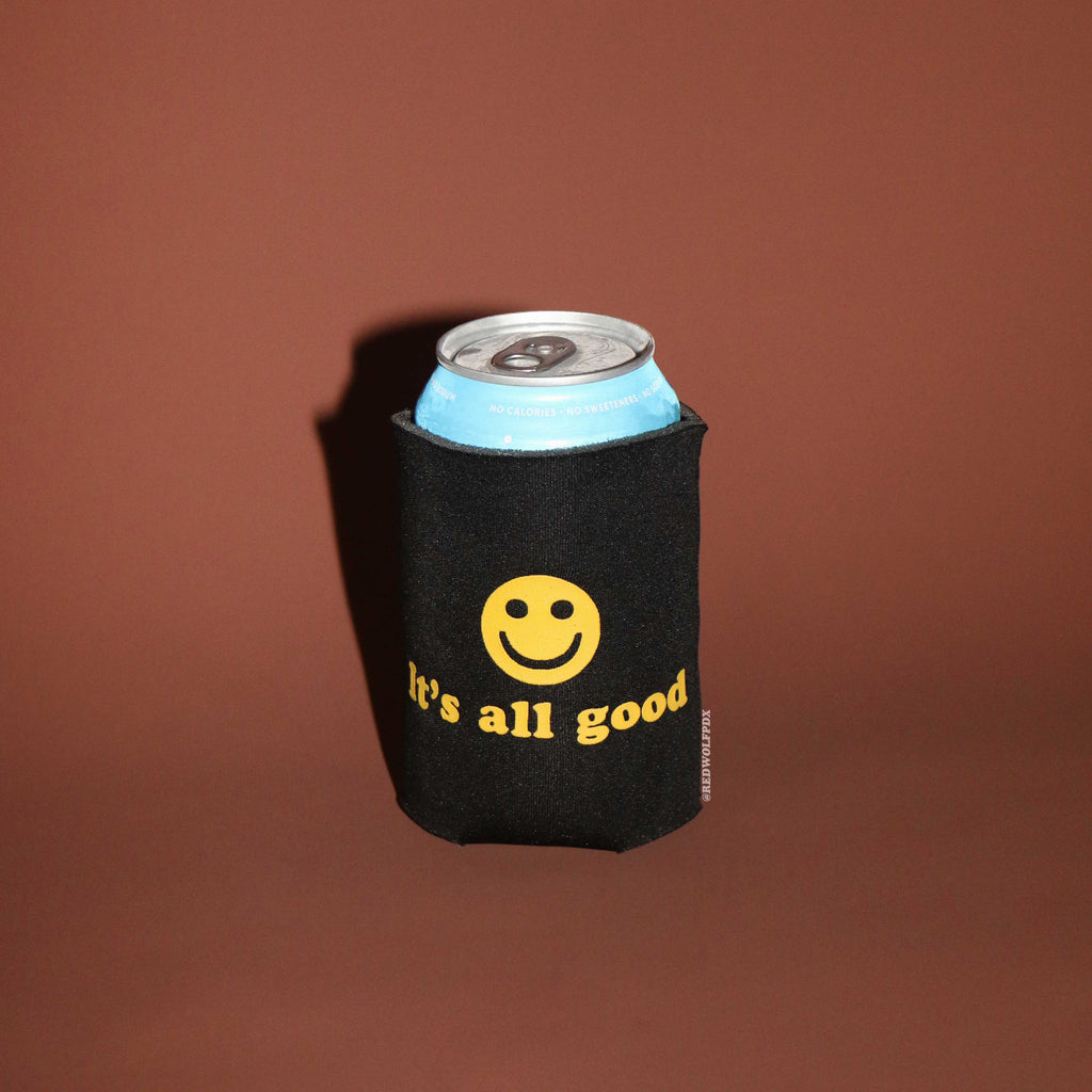 Black can cooler with yellow smiley face and 'it's all good' text on a brown background