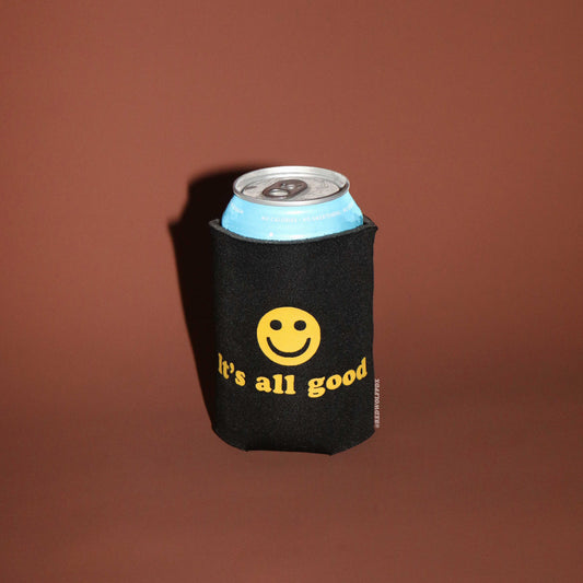 Black can cooler with yellow smiley face and 'it's all good' text on a brown background