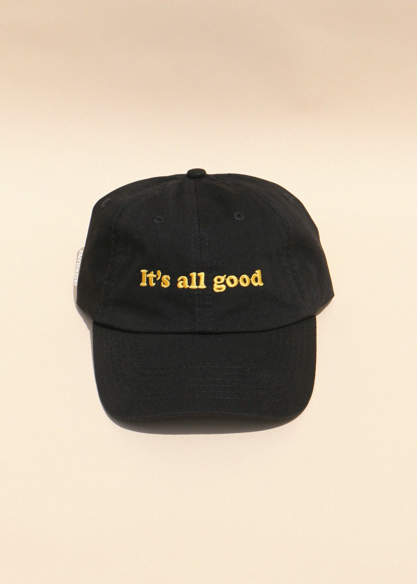 Black cap with 'It's all good' text in yellow on a beige background