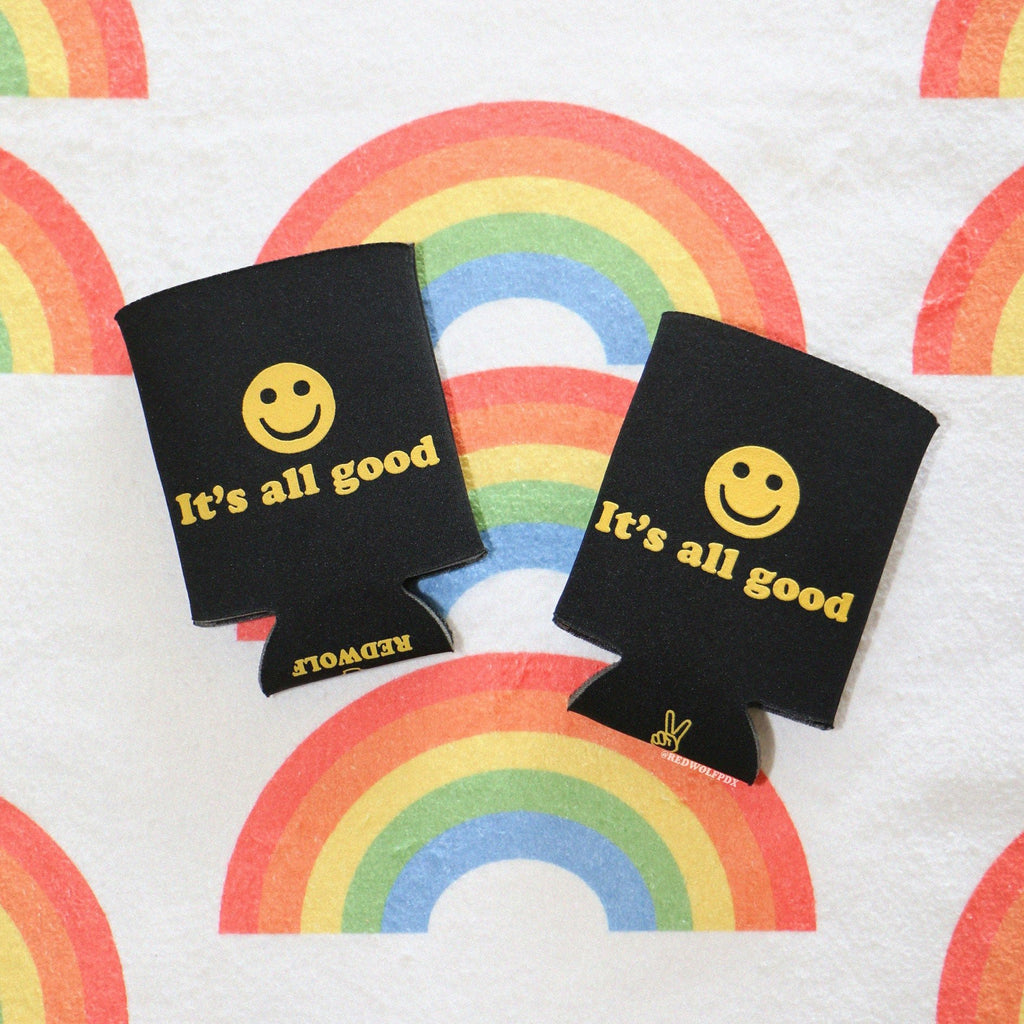 2 black neoprene drink sleeves with text 'It's all good' with smiley face graphic in yellow ink screen printed across on a rainbow background
