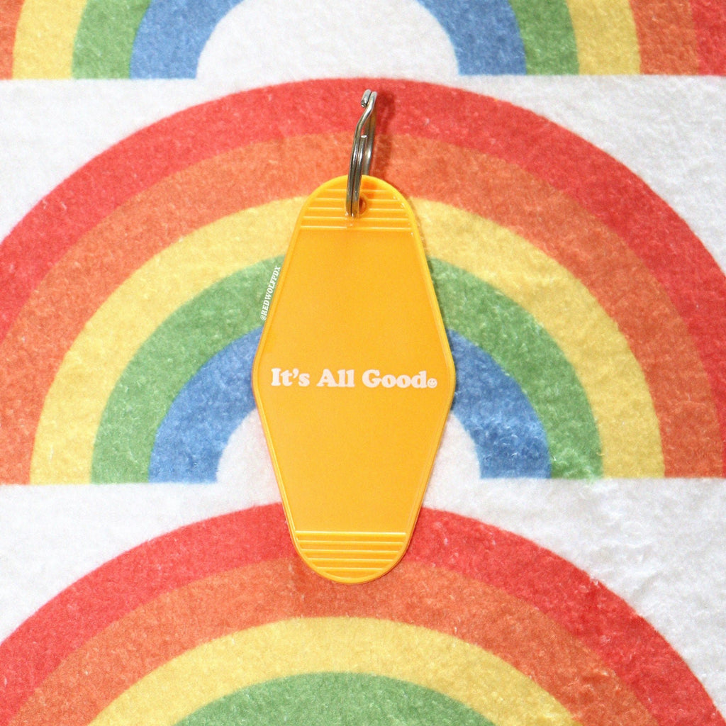 yellow retro motel style keychain with text 'It's All good' with a smiley face graphic in white ink printed across front against a rainbow background