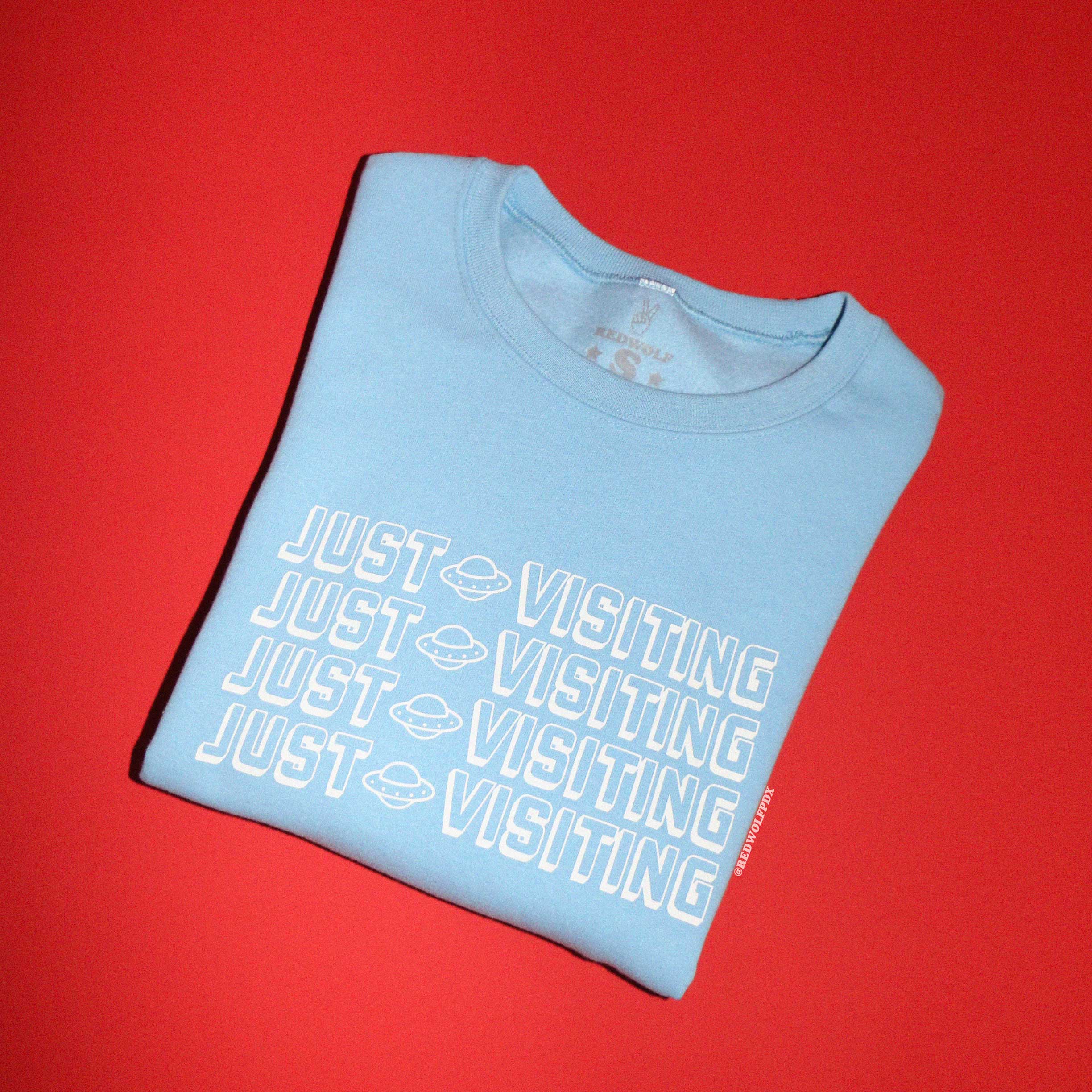 A vintage baby blue sweatshirt with the text 'JUST VISITING' printed in white across the front.