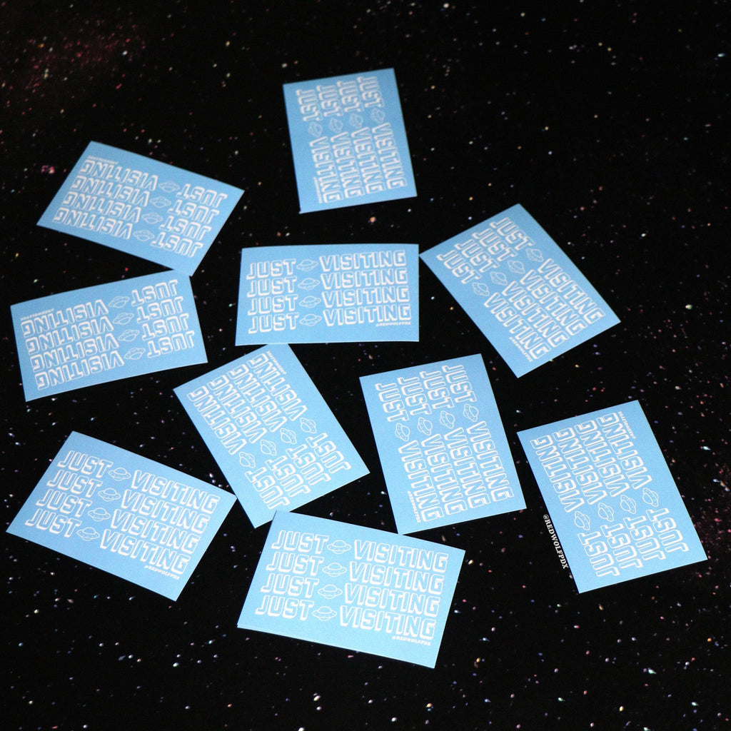 baby blue rectangle stickers with text 'JUST VISITING' printed across in white ink scattered across a space background
