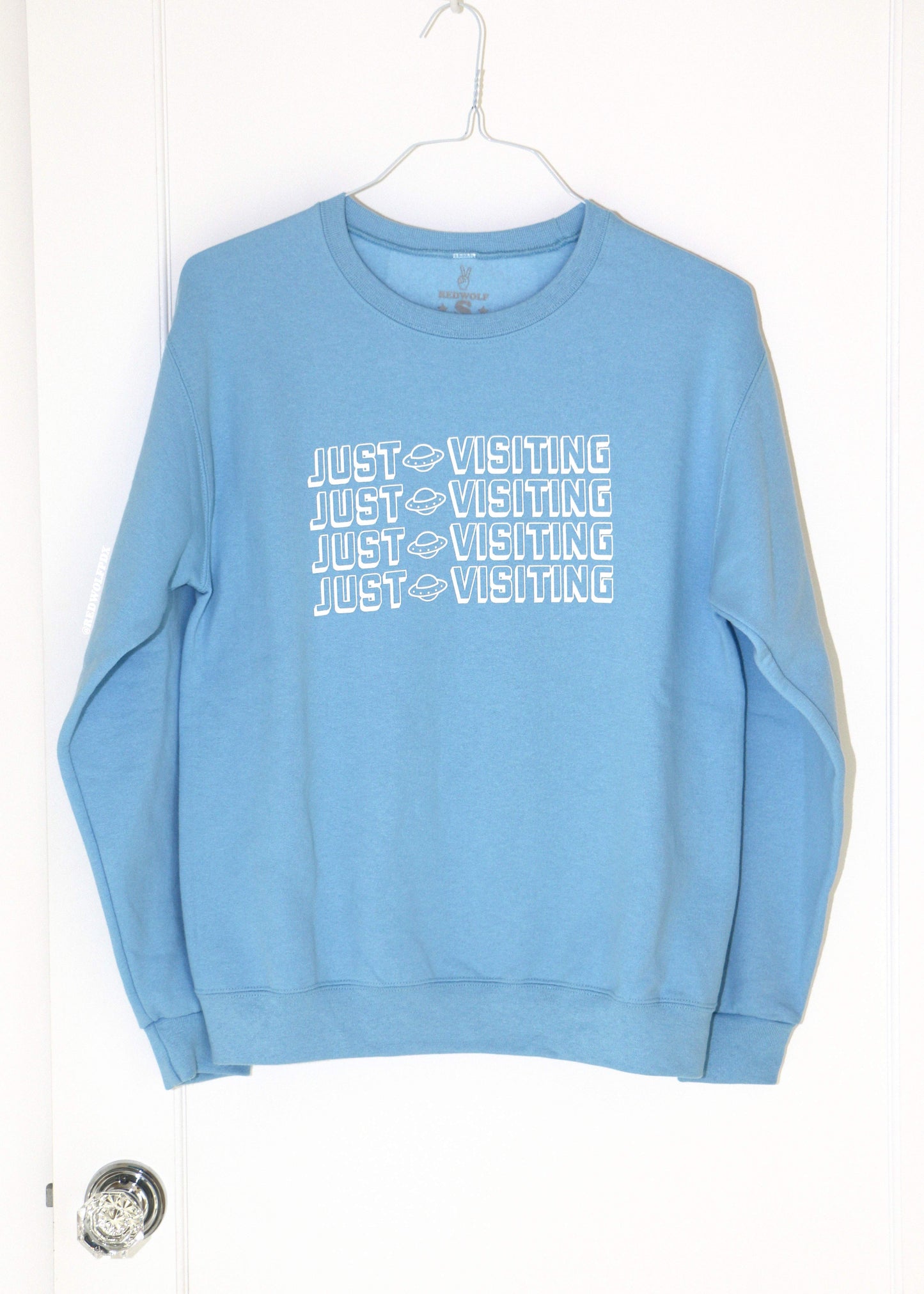 Blue sweatshirt with 'JUST VISITING' text on a white background