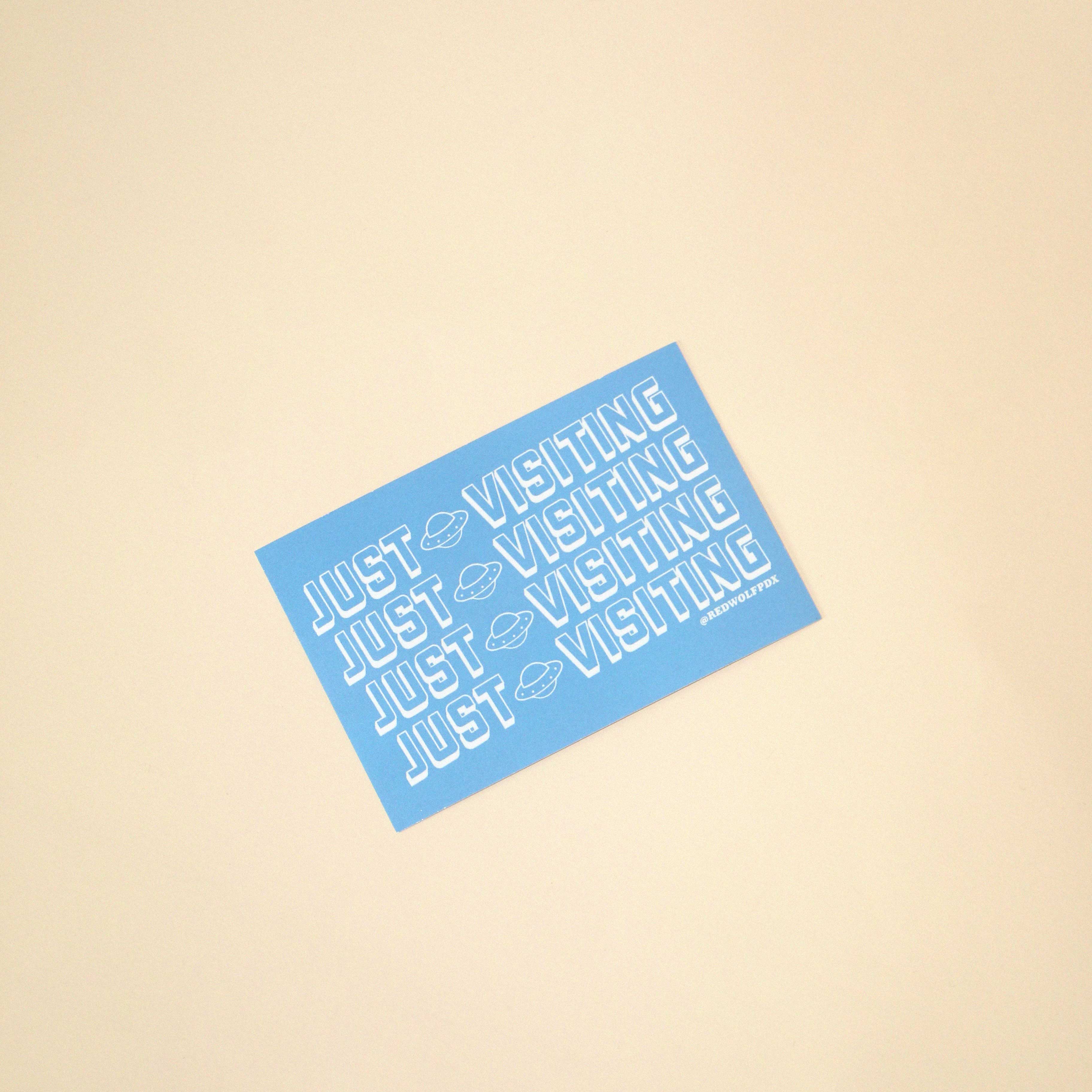 Blue sticker with 'JUST VISITING' text on a beige background