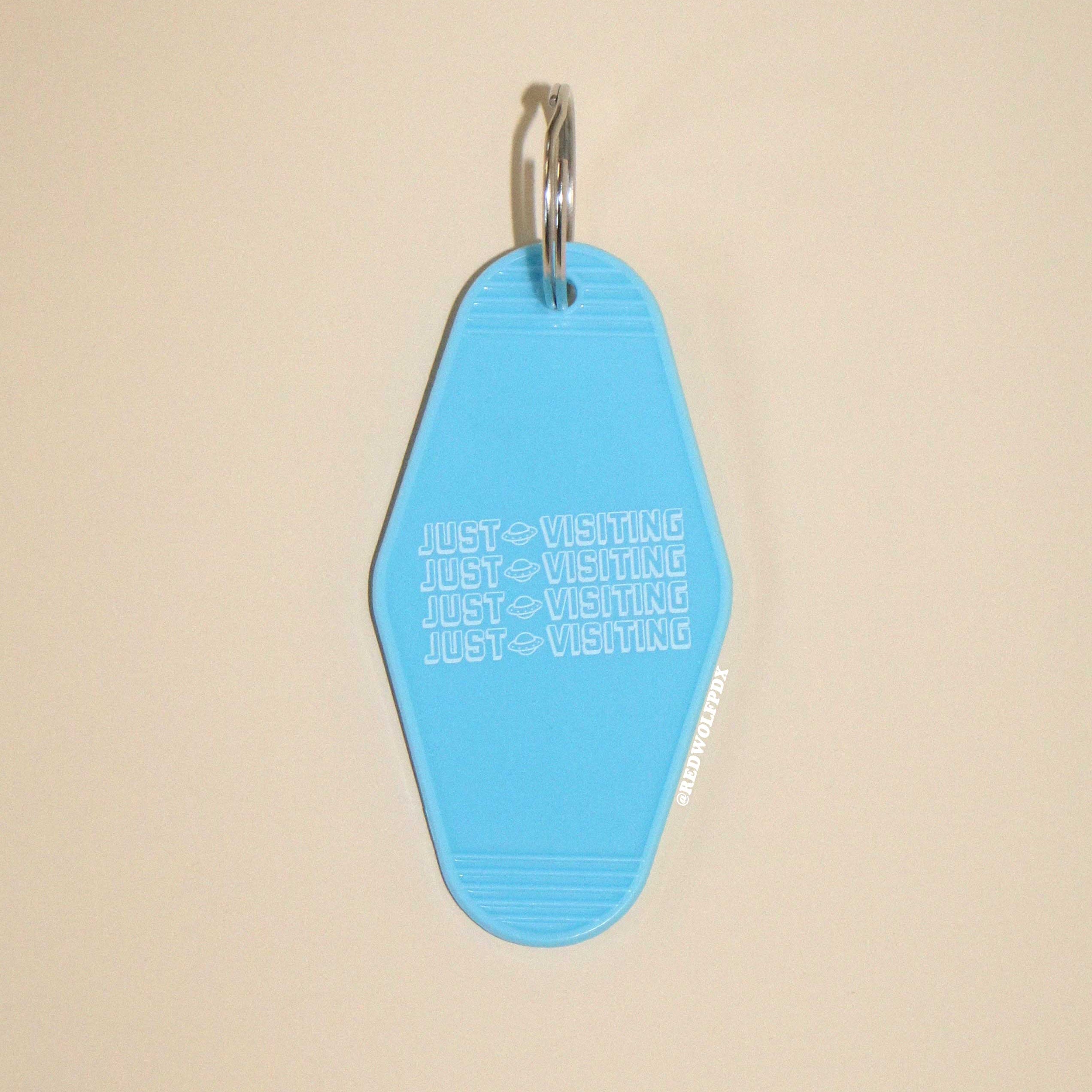 baby blue retro motel keychain with text 'JUST VISITING' in white ink printed across on a beige background