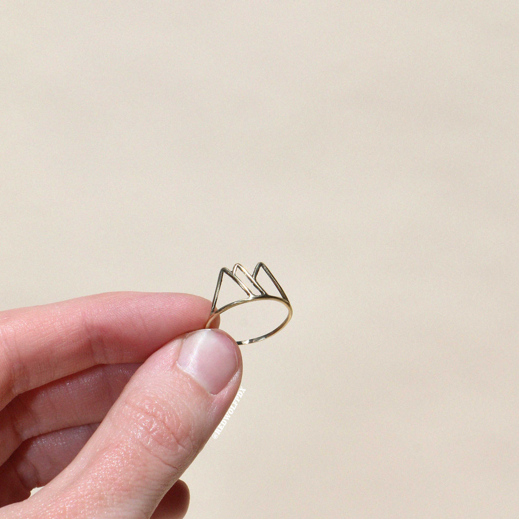 brass mountain outline ring being held against a beige backdrop