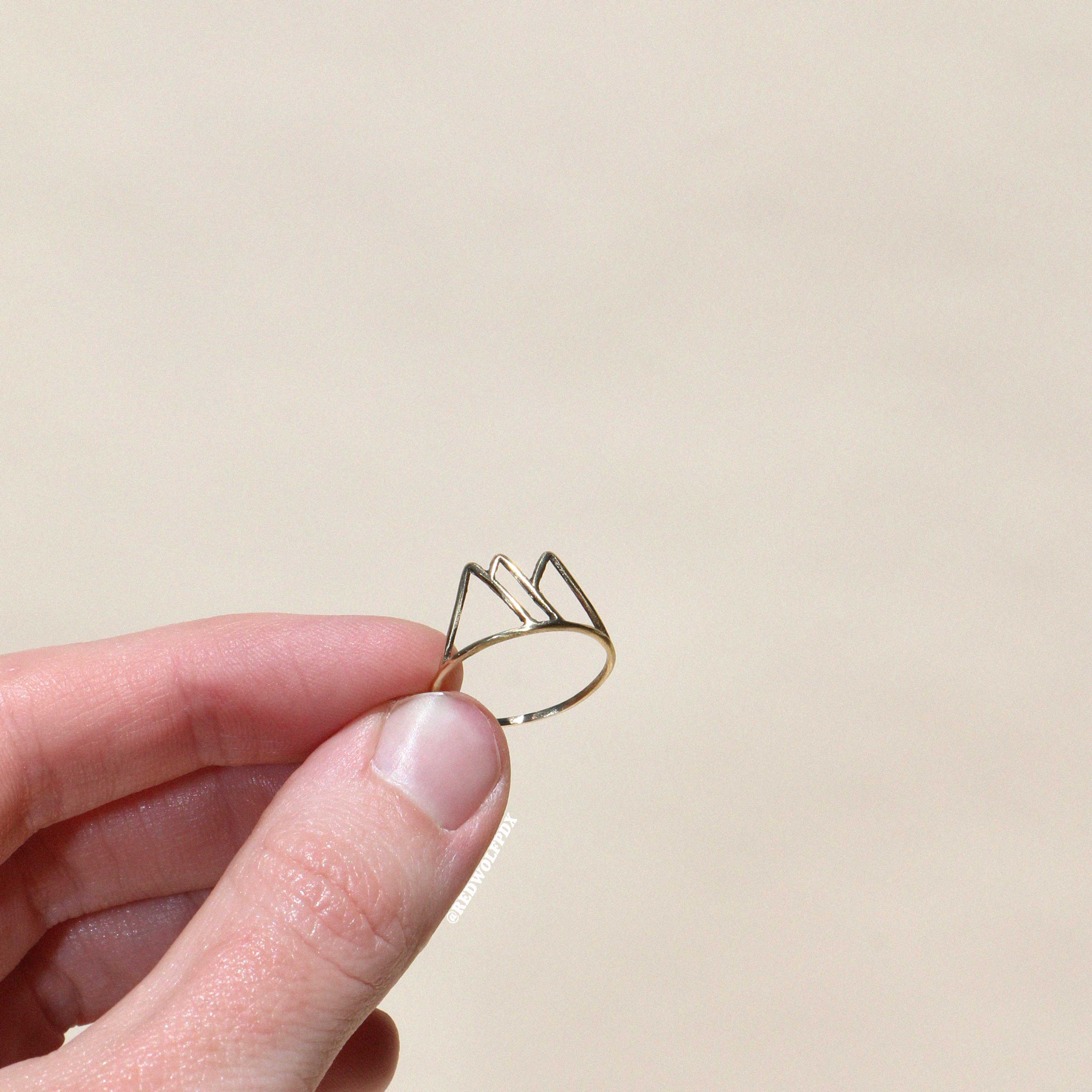 brass mountain outline ring being held against a beige backdrop
