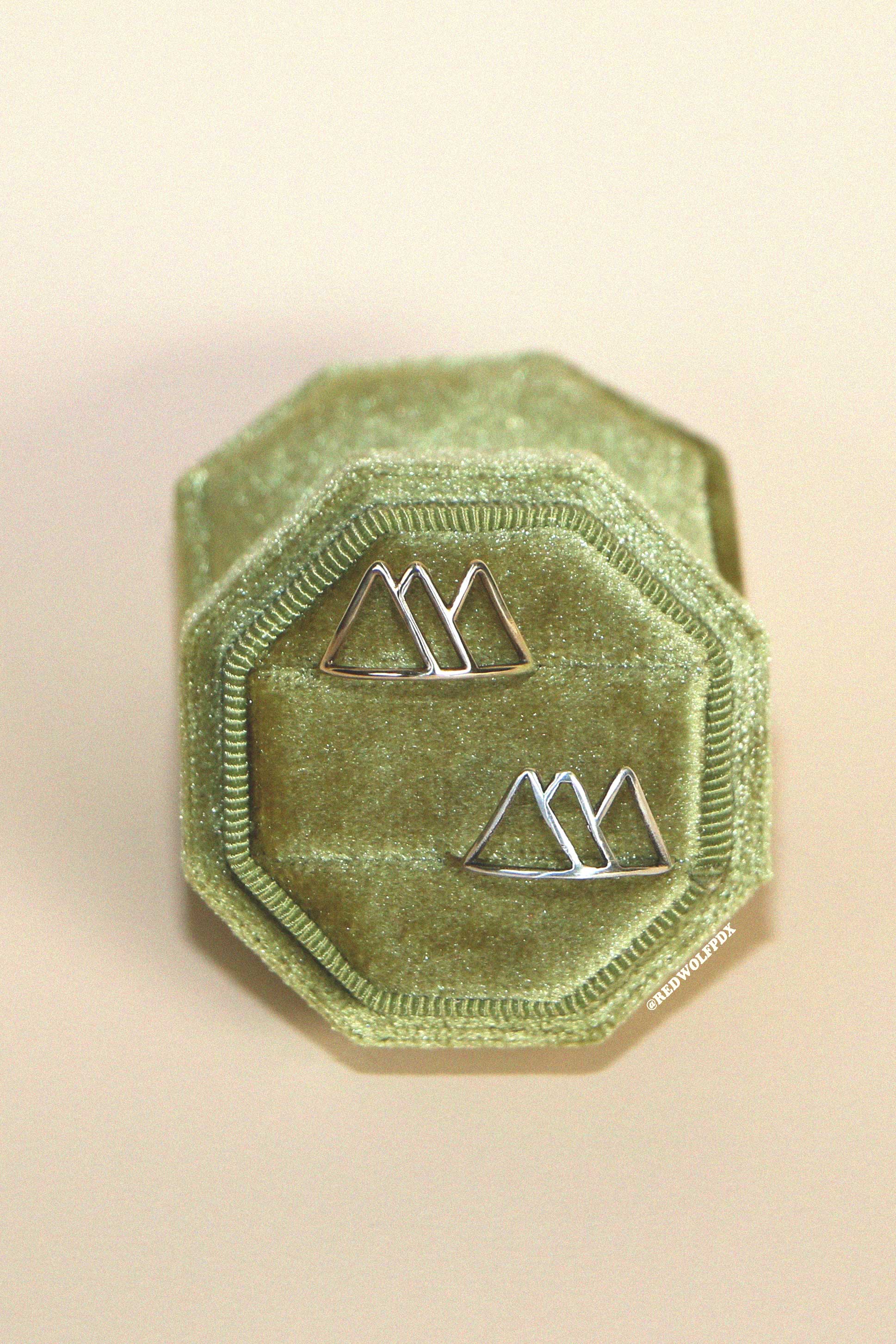 A sterling silver ring  and brass ring with a mountain outline design, displayed on a green velvet surface.