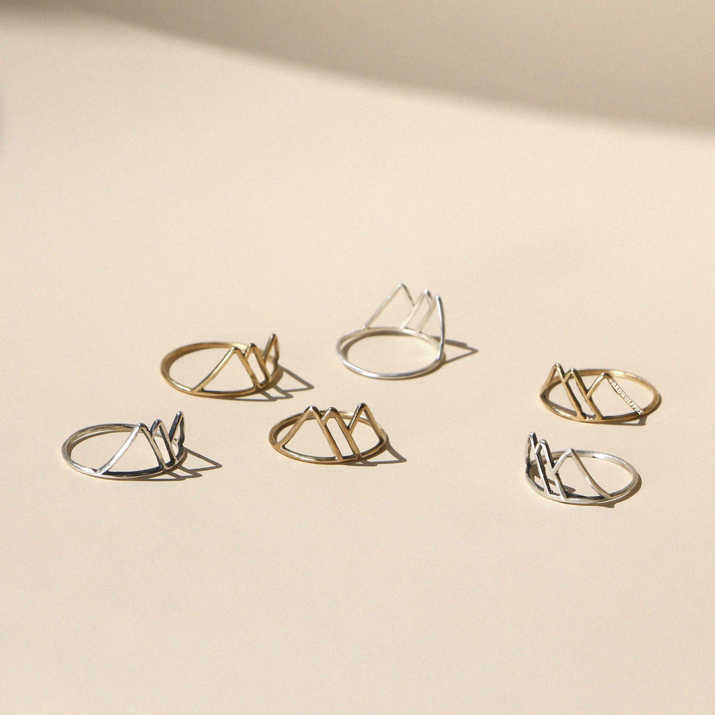A collection of mountain-shaped rings in  sterling silver and brass, displayed against a neutral background.