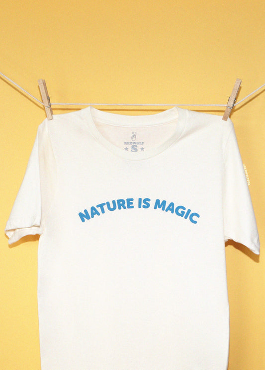 cream tee with text 'Nature is magic' screen printed across the chest in a bright blue hanging on a clothing line against a yellow backdrop.