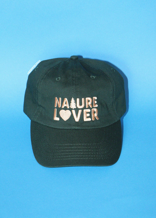 A dark green baseball cap with 'NATURE LOVER' embroidered on the front in beige, featuring a small pine tree and heart symbol, set against a solid blue background.