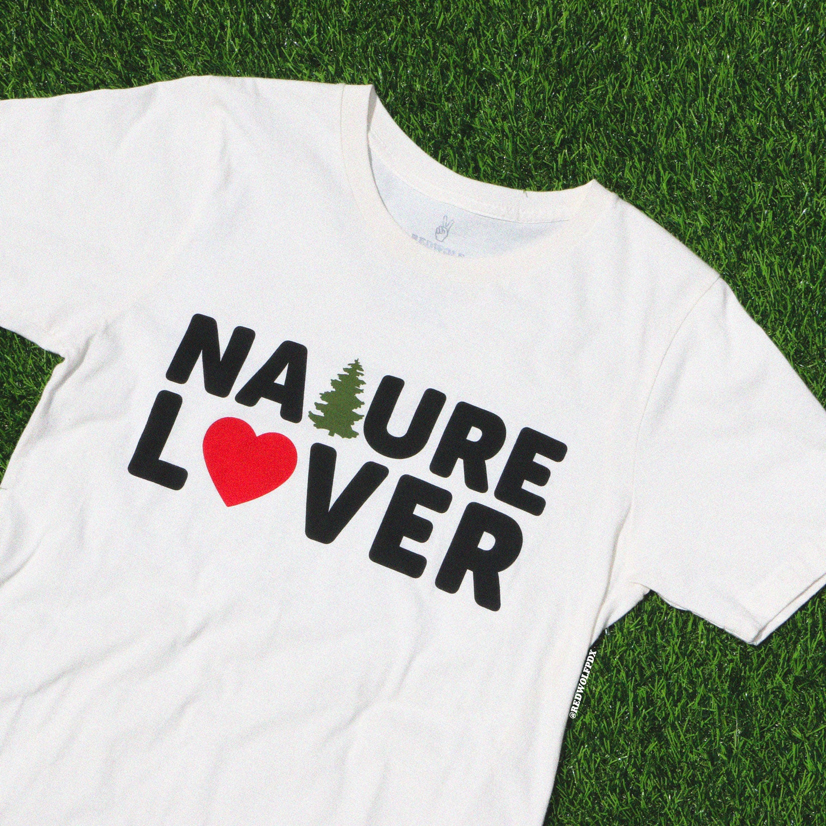 beige graphic tee with text 'NATURE LOVER' screen printed across front on green grass background