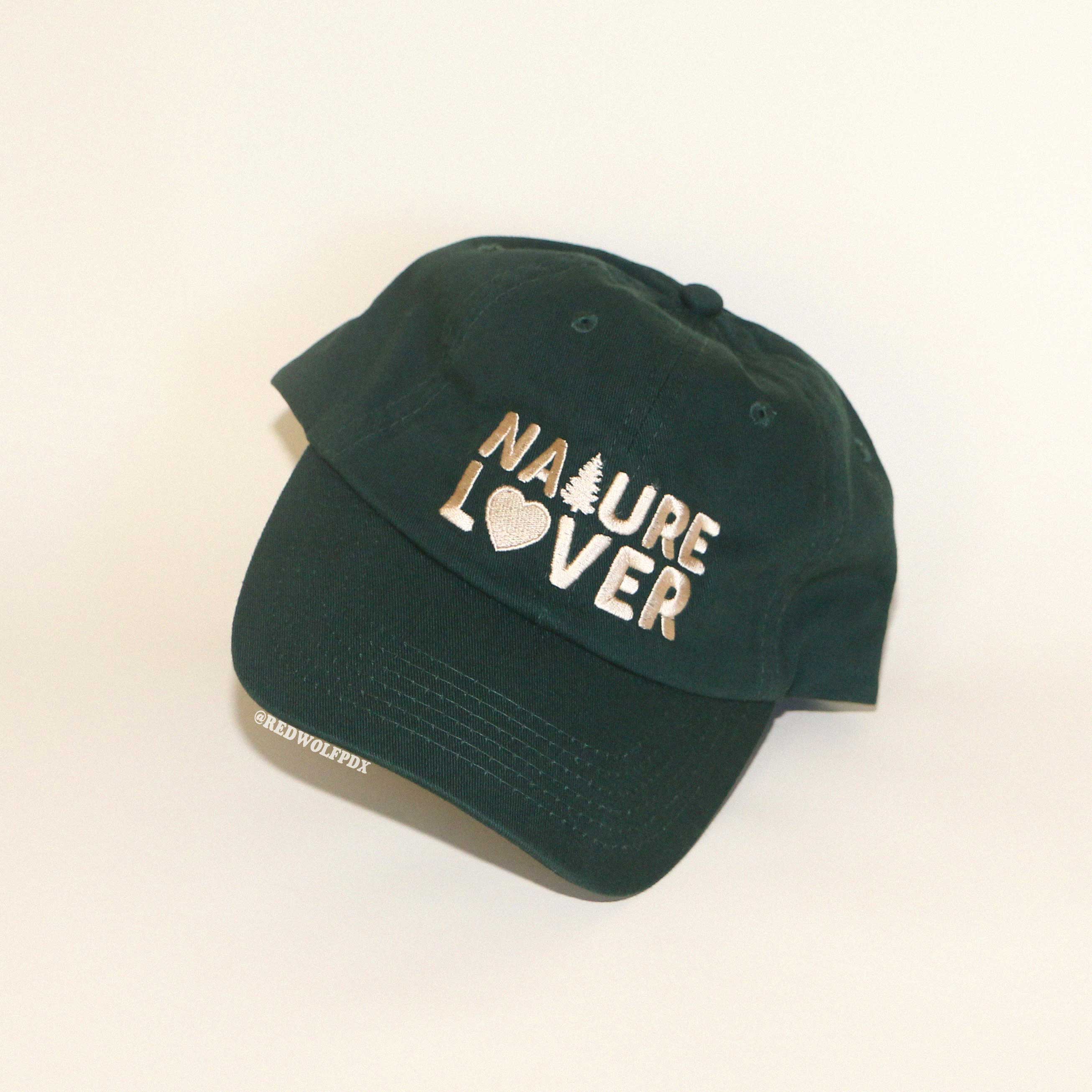 forest green baseball cap with text 'NATURE LOVER' embroidered across the front against a beige backdrop
