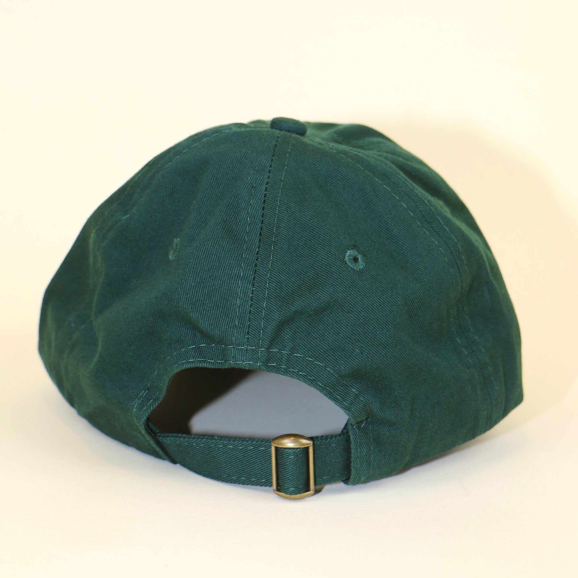 back of forest green baseball cap with adjustable brass buckle on a beige backdrop