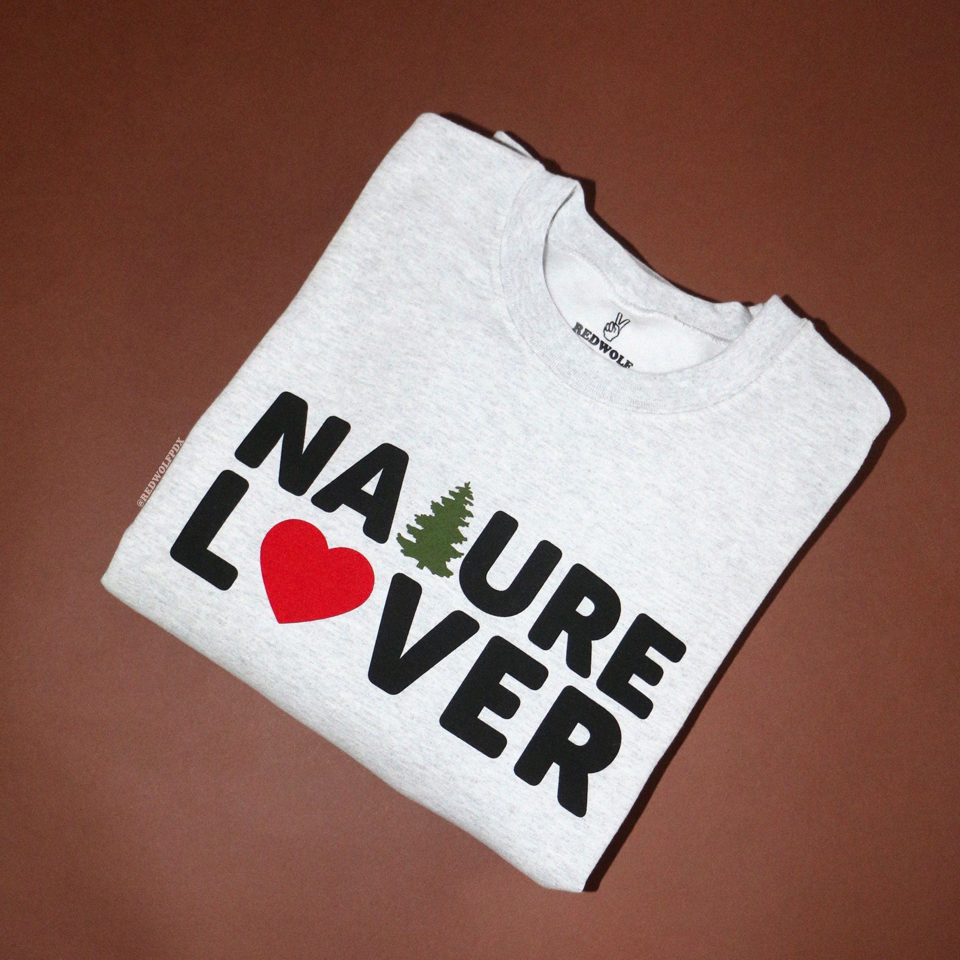 Gray folded crewneck sweatshirt with text 'NATURE LOVER' across chest on brown backdrop