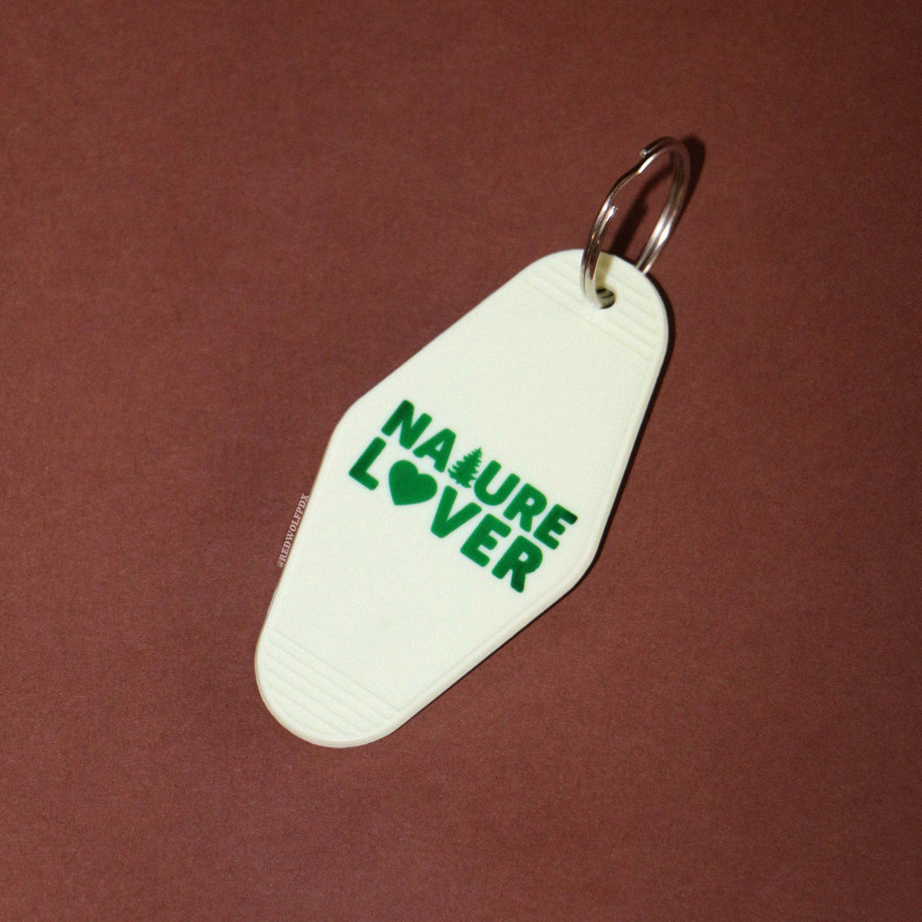 A vintage white keychain with the text 'NATURE LOVER' in dark green, shaped like a motel key on a brown backdrop