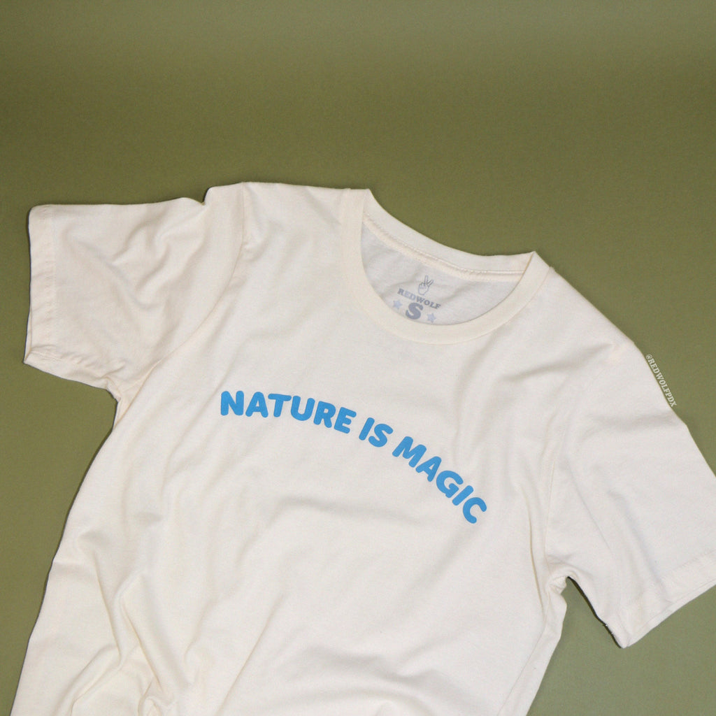 beige graphic tee with text 'NATURE IS MAGIC' in blue ink across chest on a vintage green background