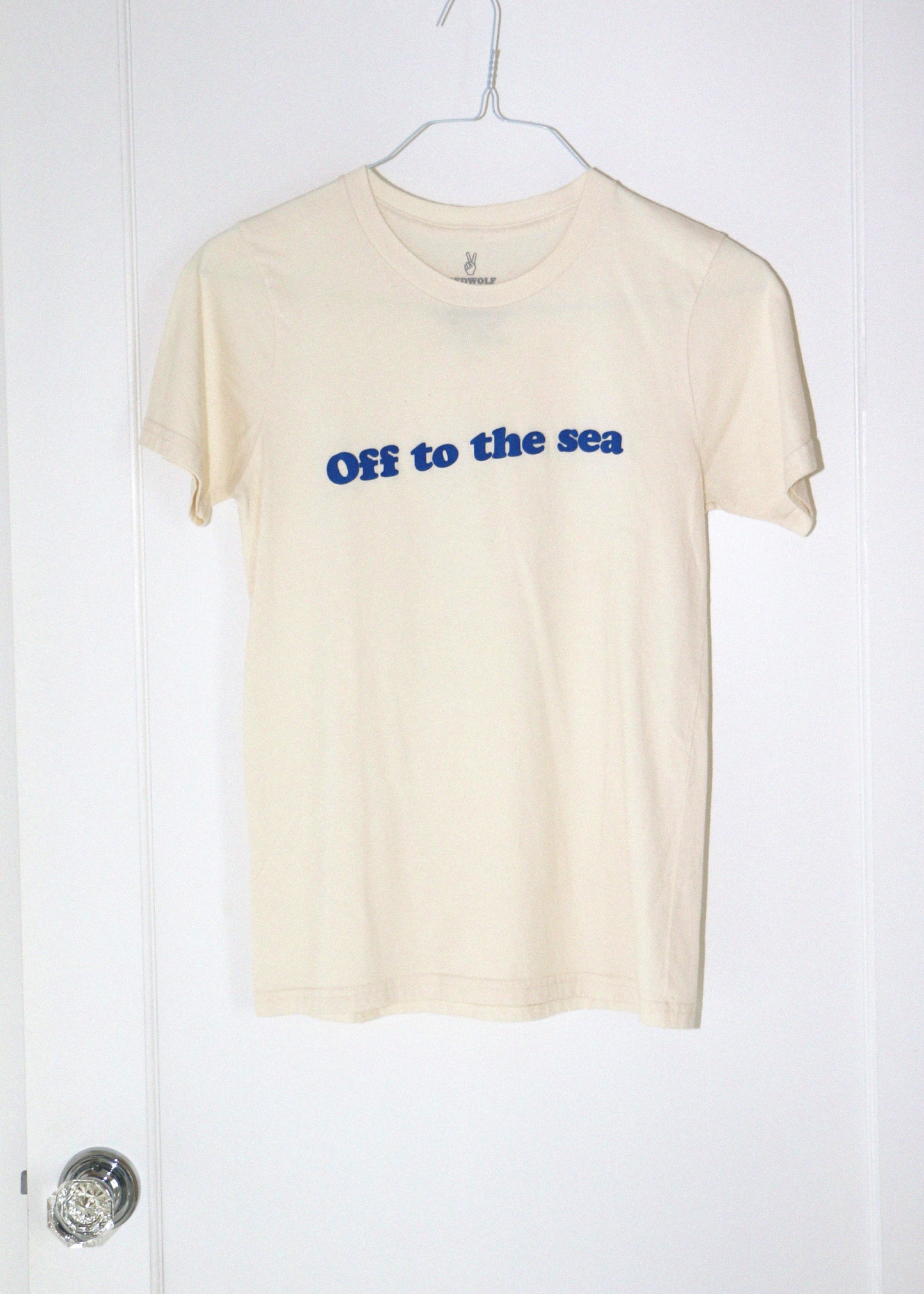 cream t-shirt with 'Off to the sea' text on a hanger against a white background
