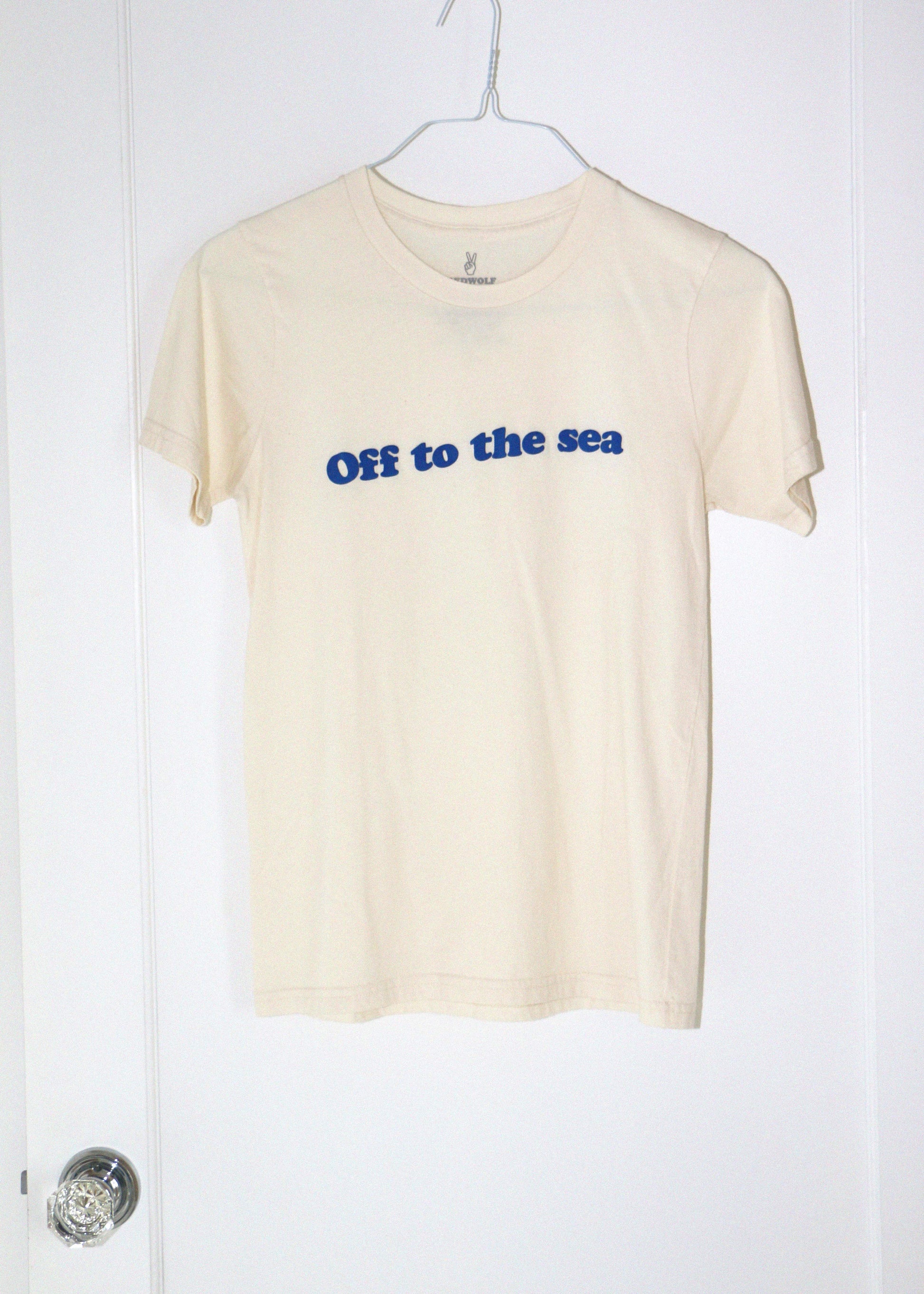 cream t-shirt with 'Off to the sea' text on a hanger against a white background