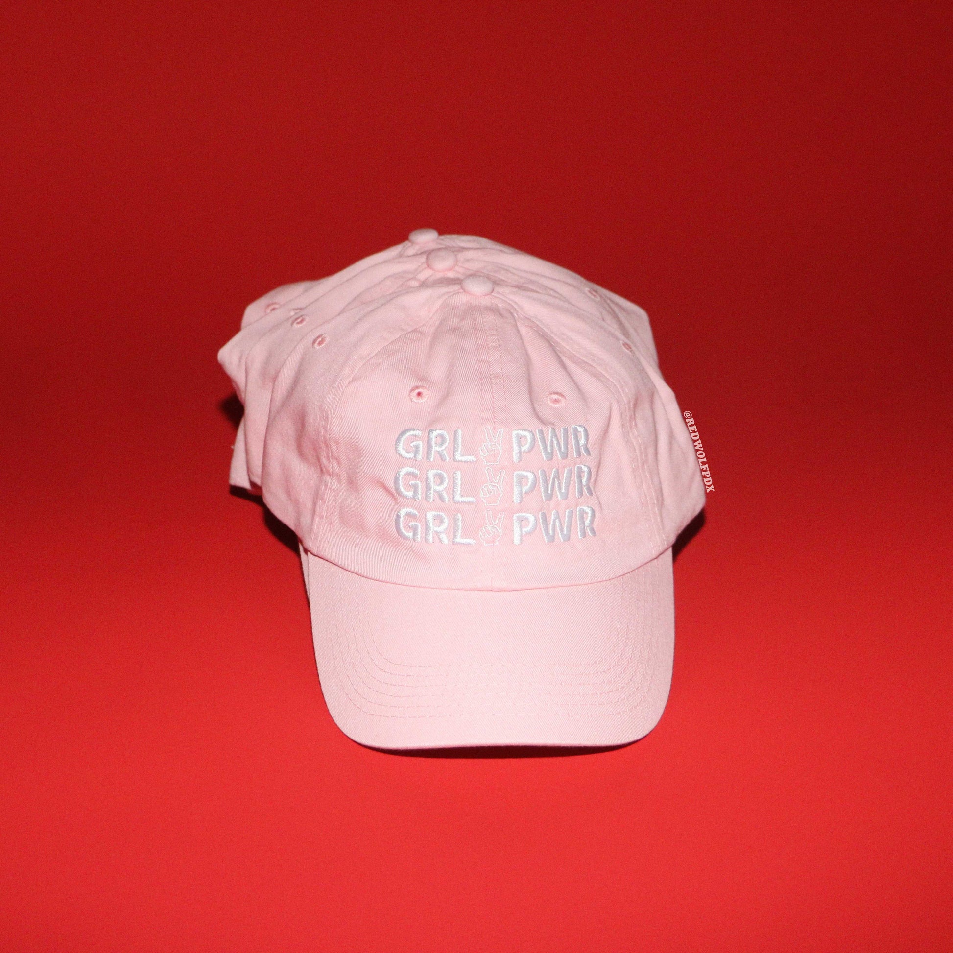 stack of pink baseball caps with 'GRL PWR' text on a red background