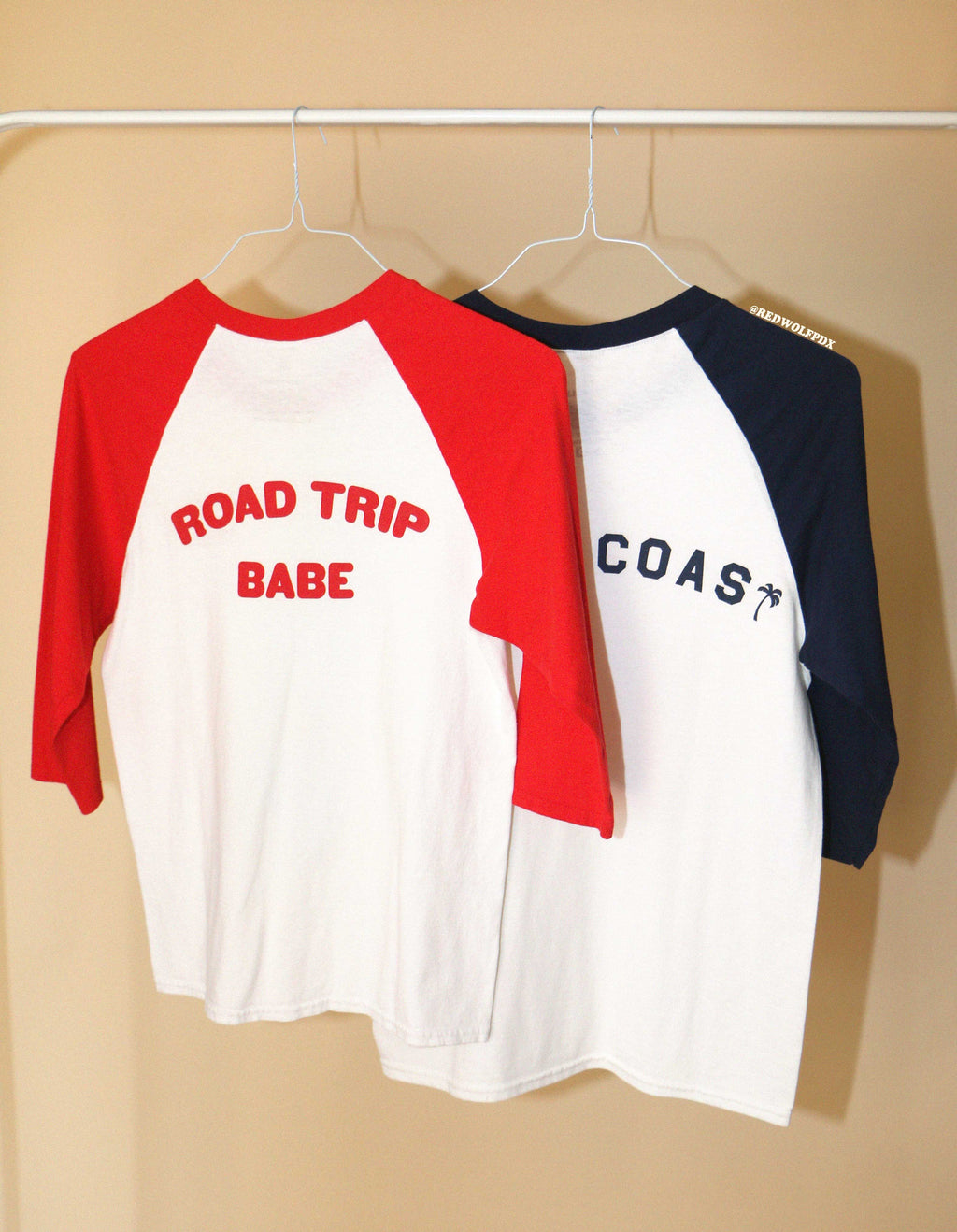 Two baseball shirts hanging on a rack with 'ROAD TRIP BABE' and 'WEST COAST' text.