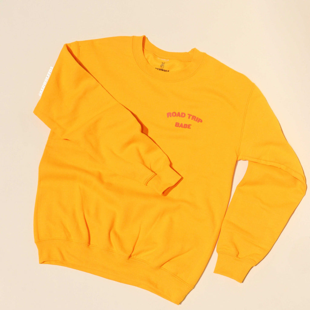 Yellow sweatshirt with 'ROAD TRIP BABE' text on a beige background