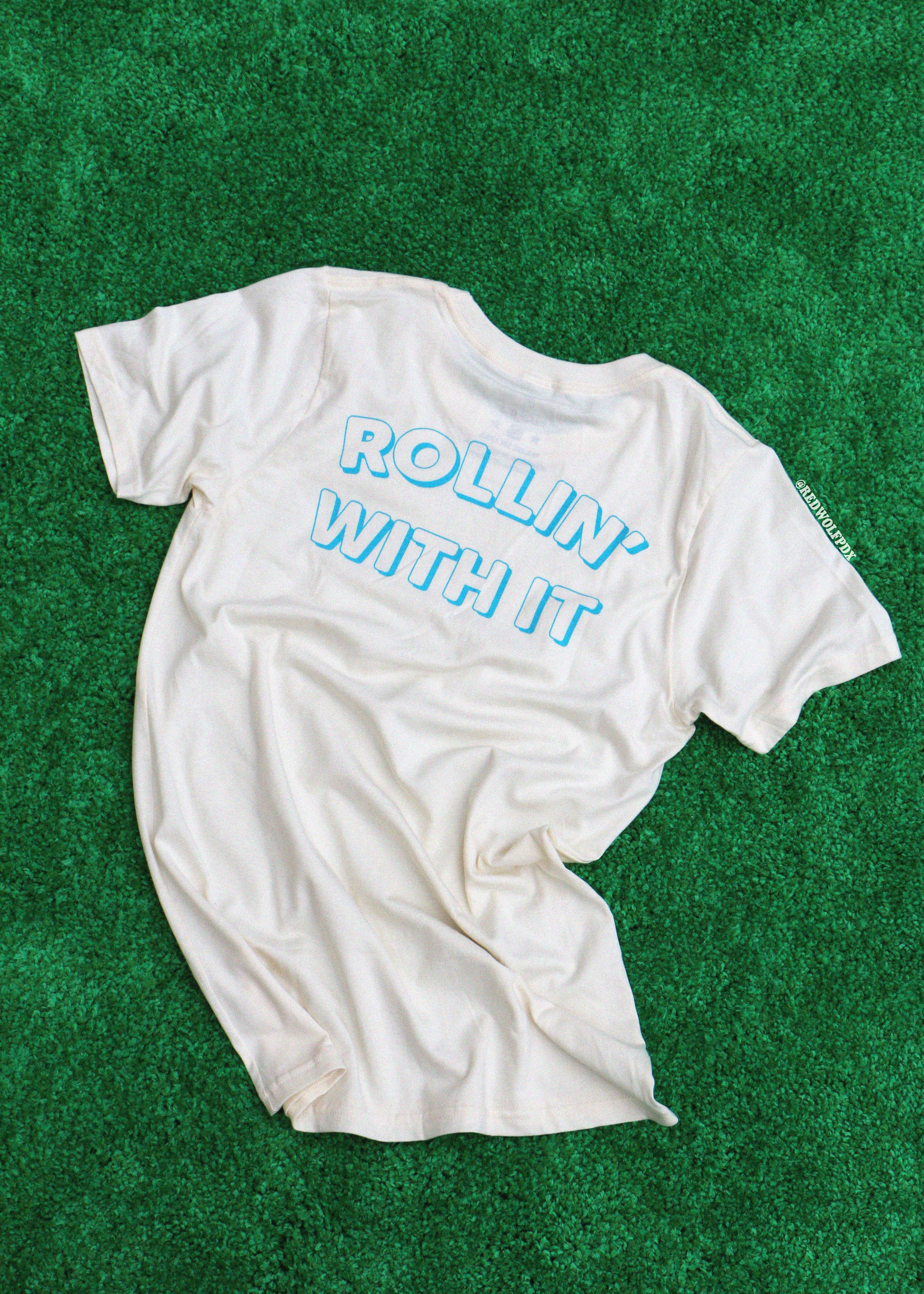 White t-shirt with 'Rollin' With It' text on a green textured background