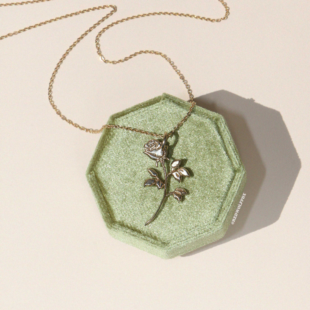 A rose necklace with a brass chain displayed on a green octagonal dish.