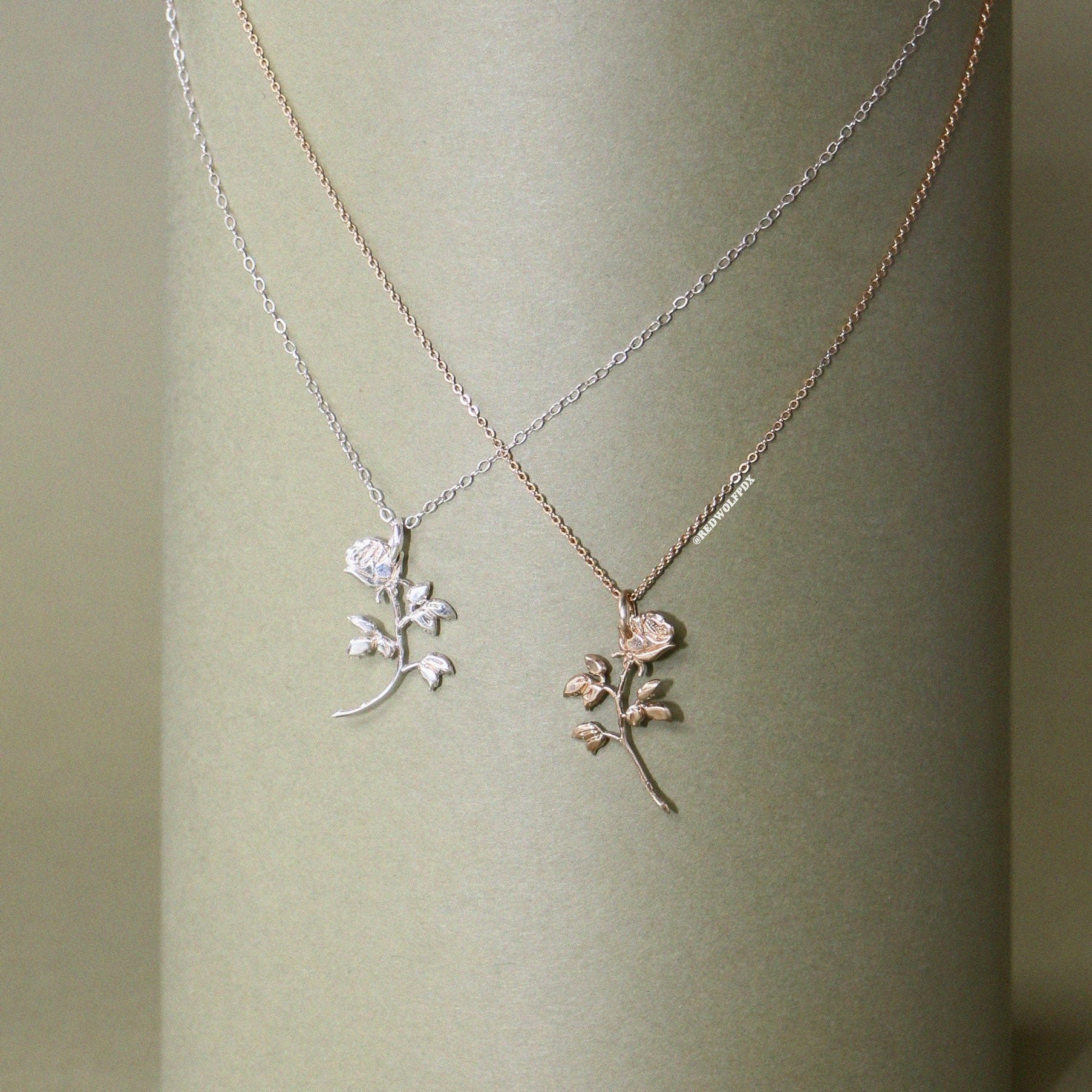 Two necklaces with rose charms, one in silver and one in brass, displayed on a vintage green backdrop