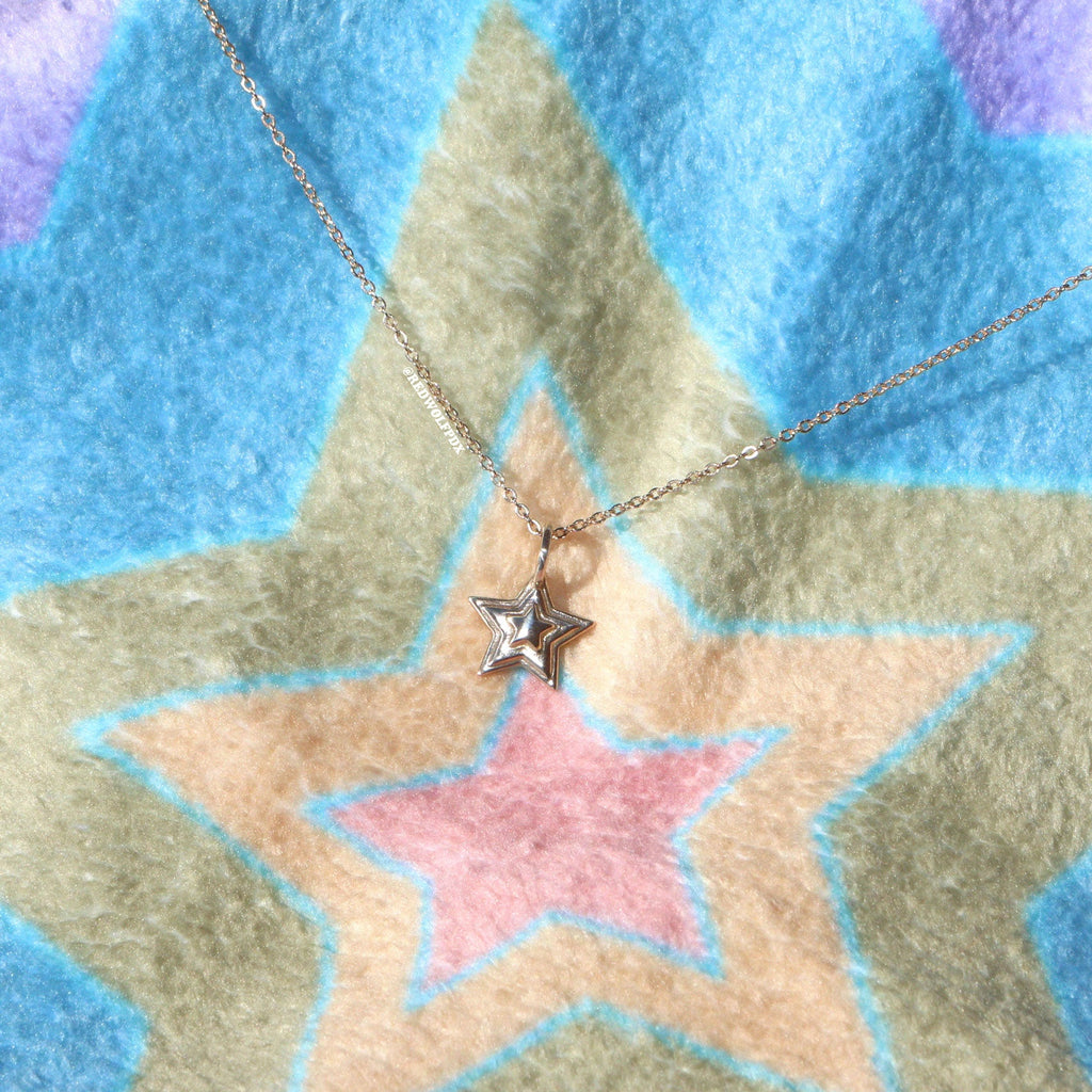 A brass 3-d layered starburst charm hanging from brass chain necklace placed on a colorful starburst backgroundcolors.