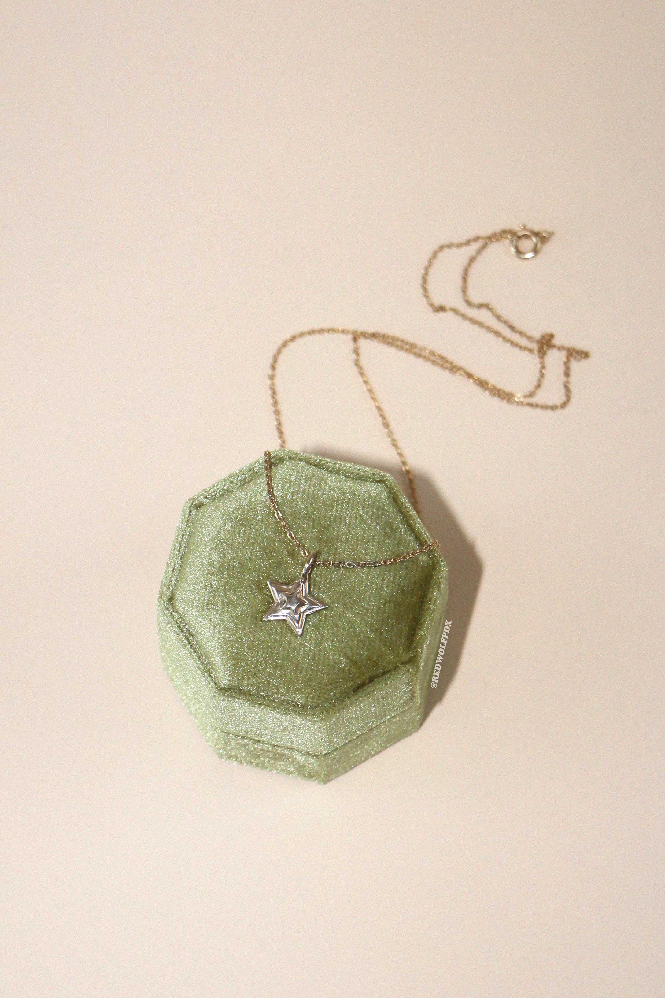 A brass starburst 3-d layered charm hanging from a brass chain necklace displayed on a green octagonal box on a beige background.