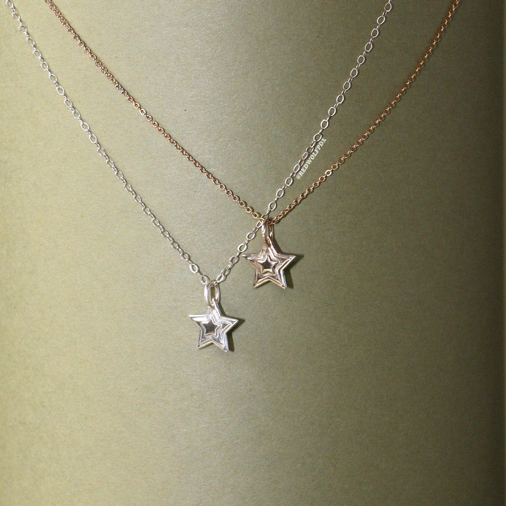 A silver and brass 3-d layered starburst charms hanging on chain , displayed against a vintage green backdrop