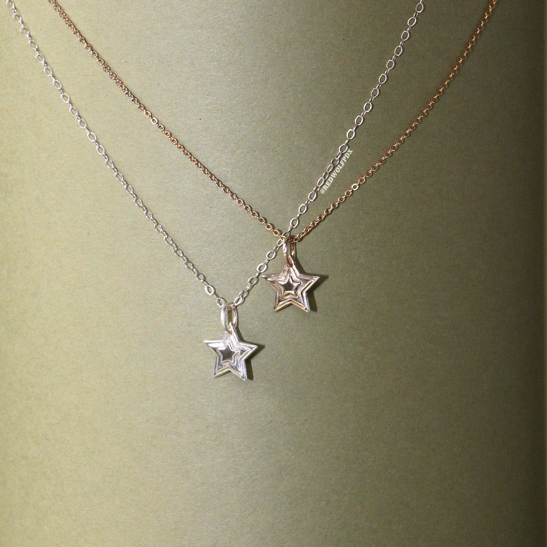 A silver and brass 3-d layered starburst charms hanging on chain , displayed against a vintage green backdrop