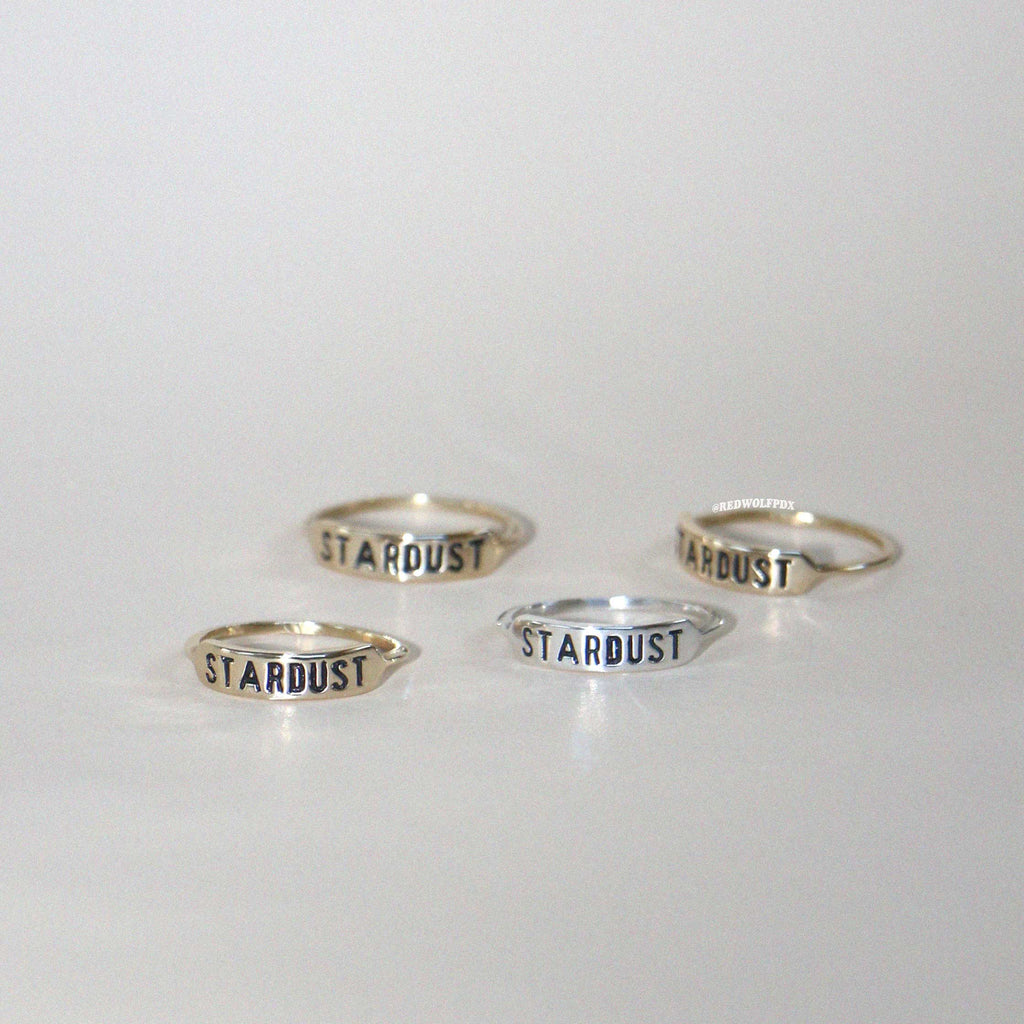 Four rings with the word 'STARDUST' engraved on them, displayed against a white background.