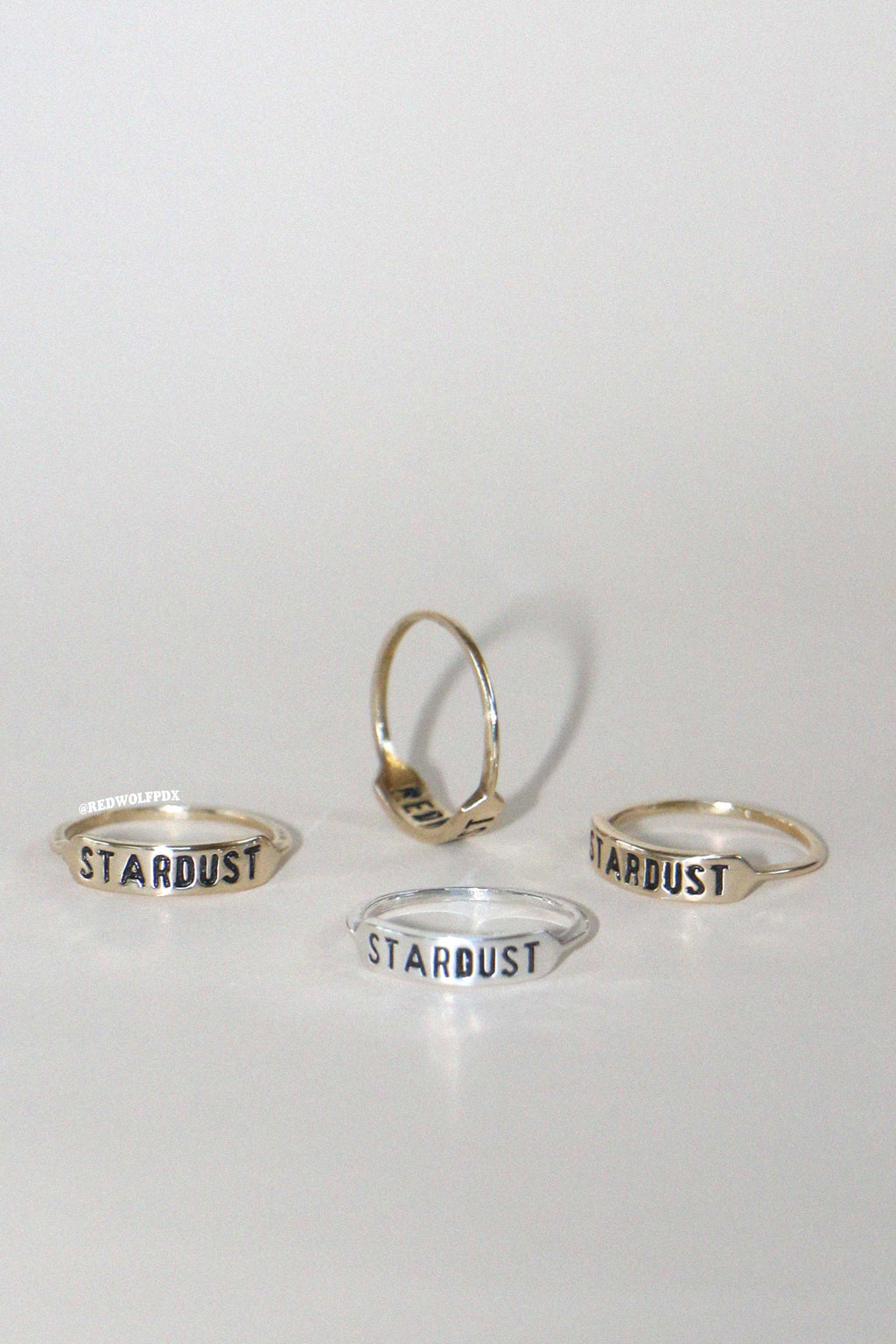 a sterling silver ring and three brass rings all with the text 'STARDUST' engraved on them scattered across a beige backdrop
